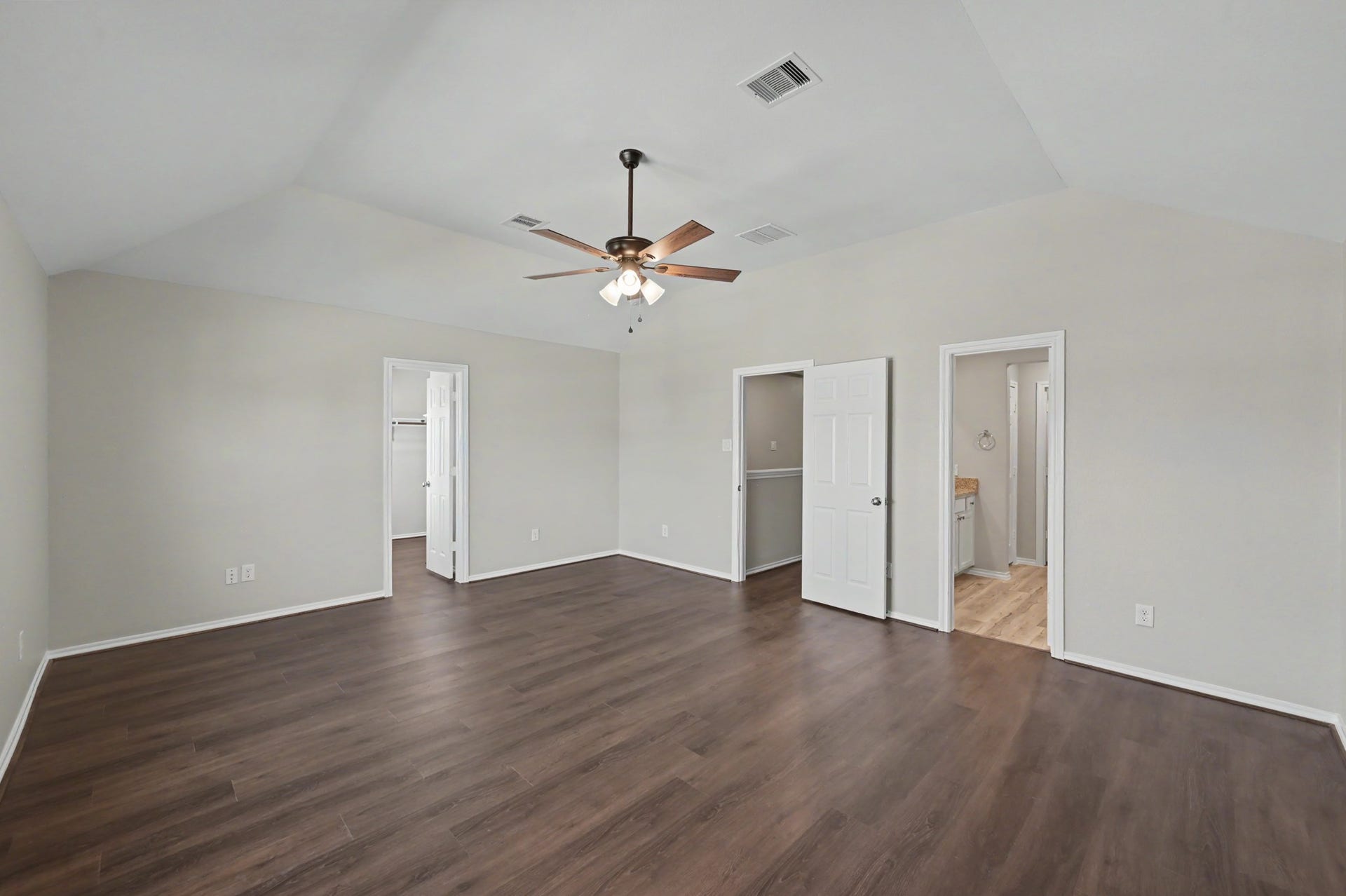 Spacious upstairs primary suite featuring vaulted ceilings, wood-look flooring, ceiling fan, walk-in closet, and private bath.