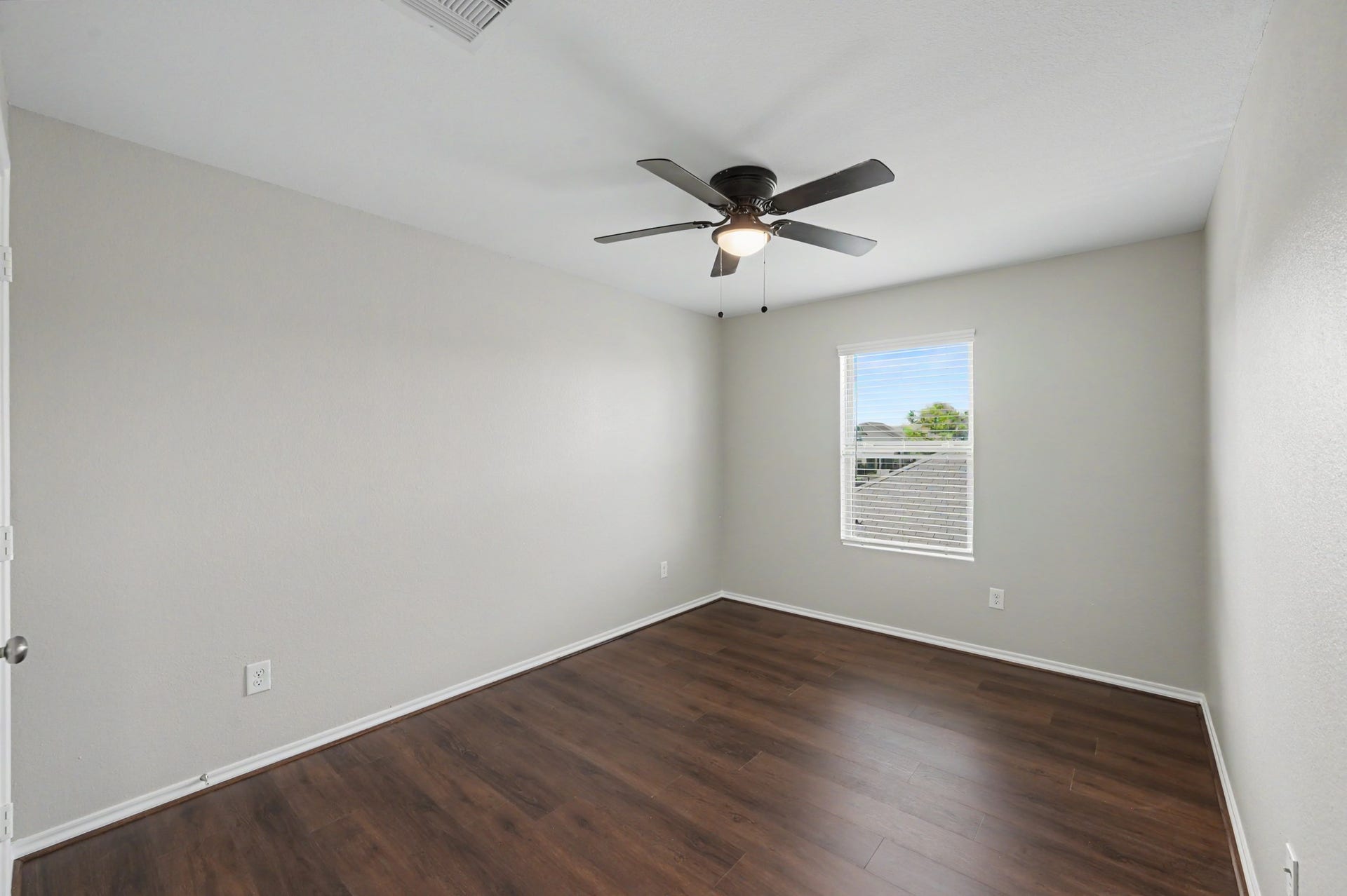 Spacious secondary bedroom featuring wood-look flooring, neutral paint tones, ceiling fan, and a large window providing natural light.