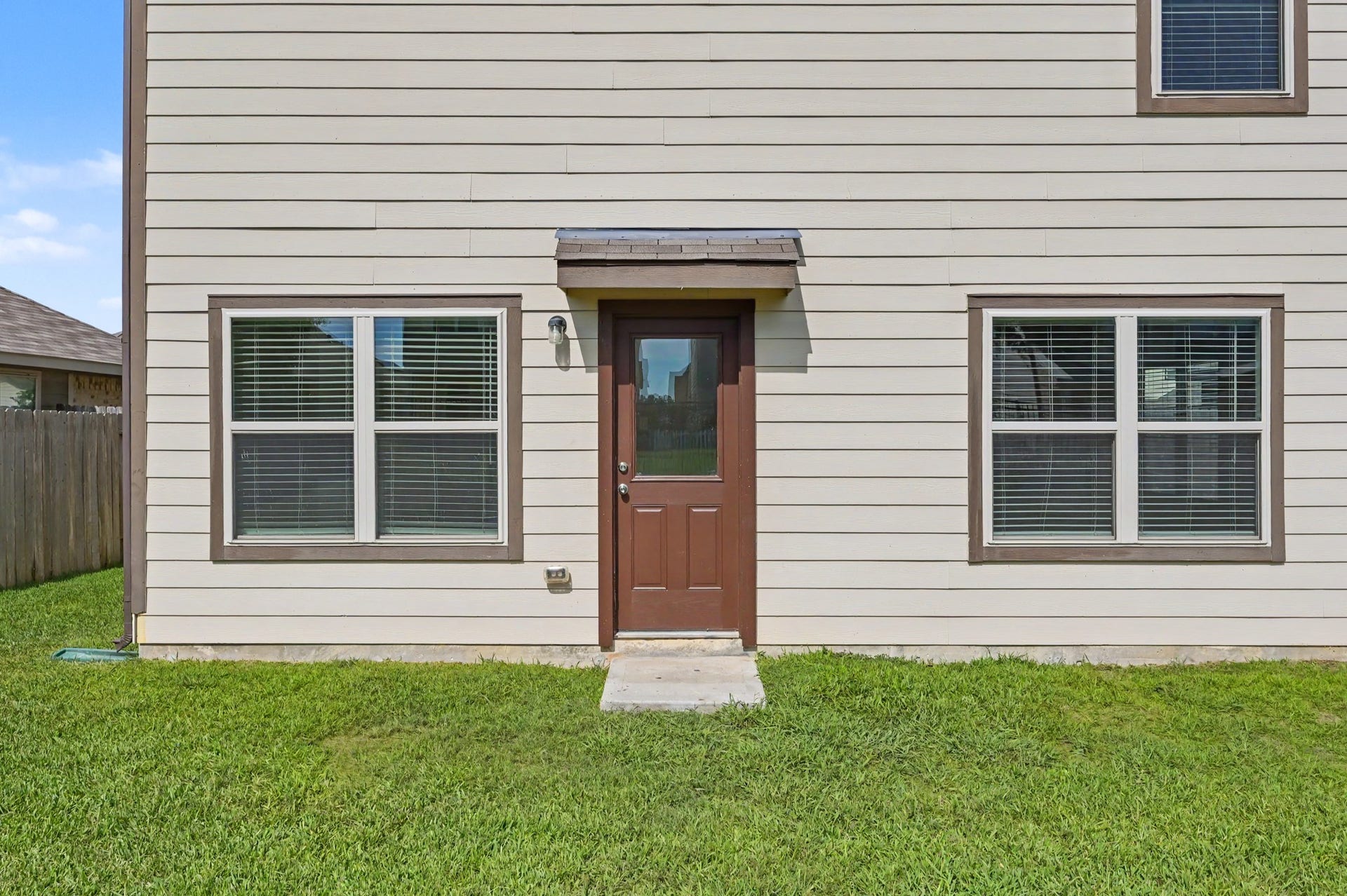 Rear exterior view featuring convenient backyard access, large windows providing natural light, and a spacious grassy yard.