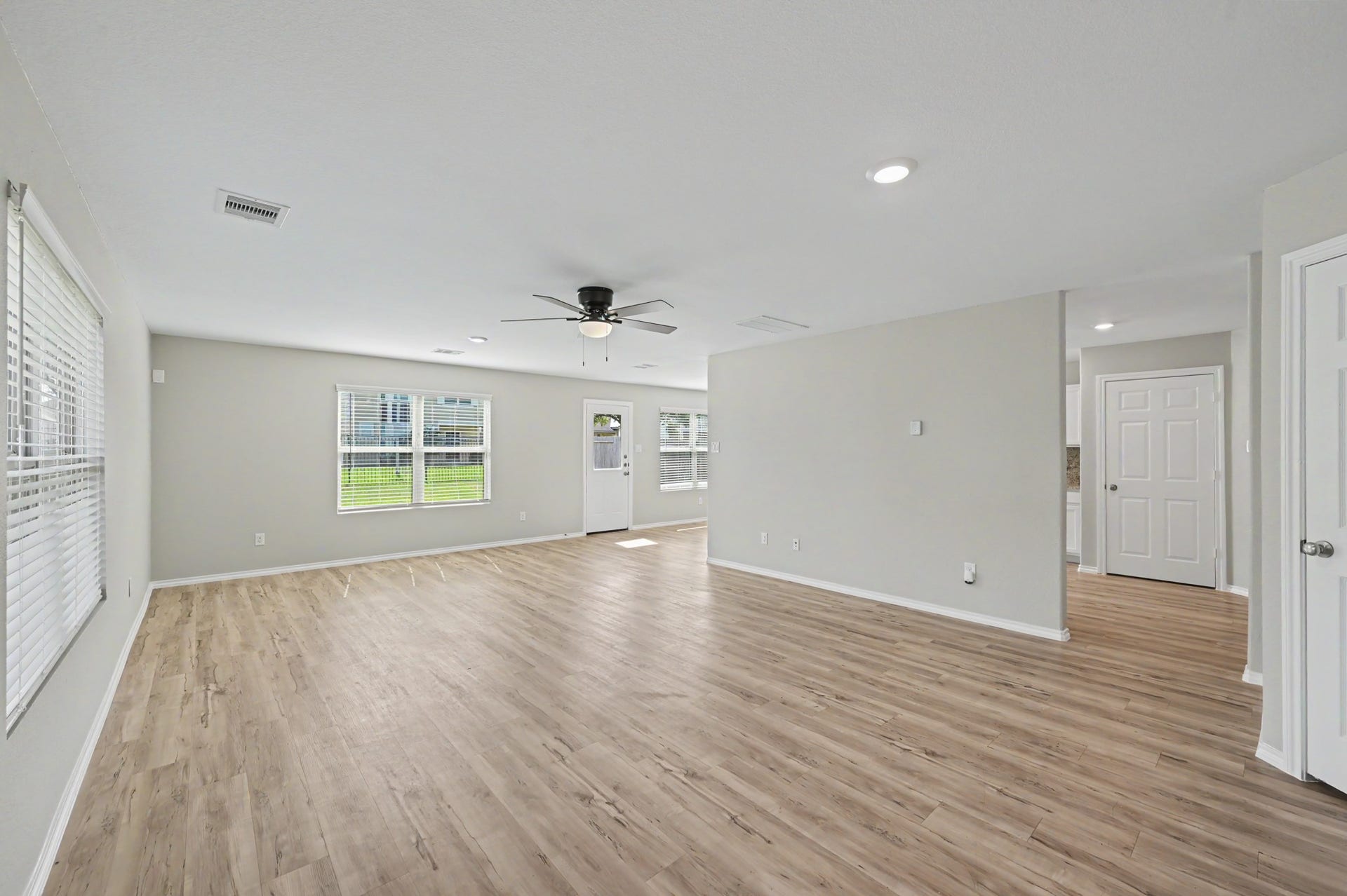 Spacious, light-filled family room featuring beautiful wood-look flooring, neutral paint tones, ceiling fan, and large windows overlooking the backyard.