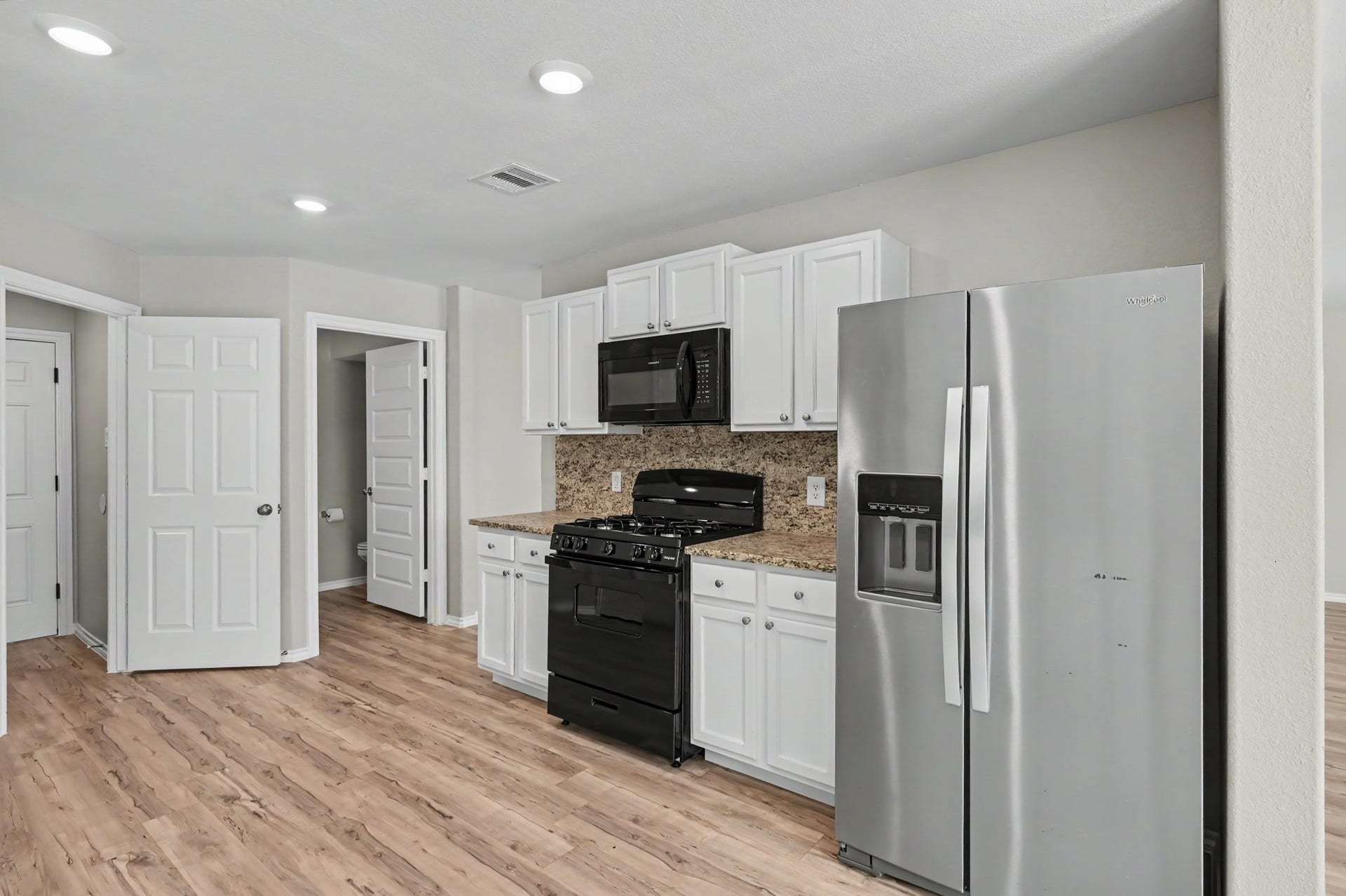 Additional kitchen view featuring white cabinetry, gas range, built-in microwave, stainless steel refrigerator, and recessed lighting.