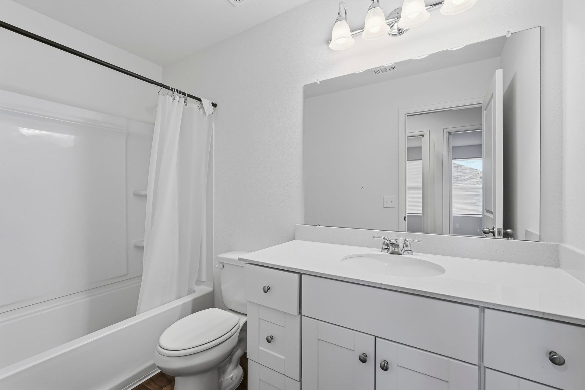 21547 Rolling Streams Drive, New Caney, TX 77357 This bright and modern full bathroom features a clean, refreshing design with crisp white walls and a timeless neutral color palette. A spacious vanity offers generous countertop space, cabinetry, and ample storage, complemented by a large wall-mounted mirror and elegant four-light fixture. The shower and bathtub combination features a white surround with built-in shelving for added convenience.