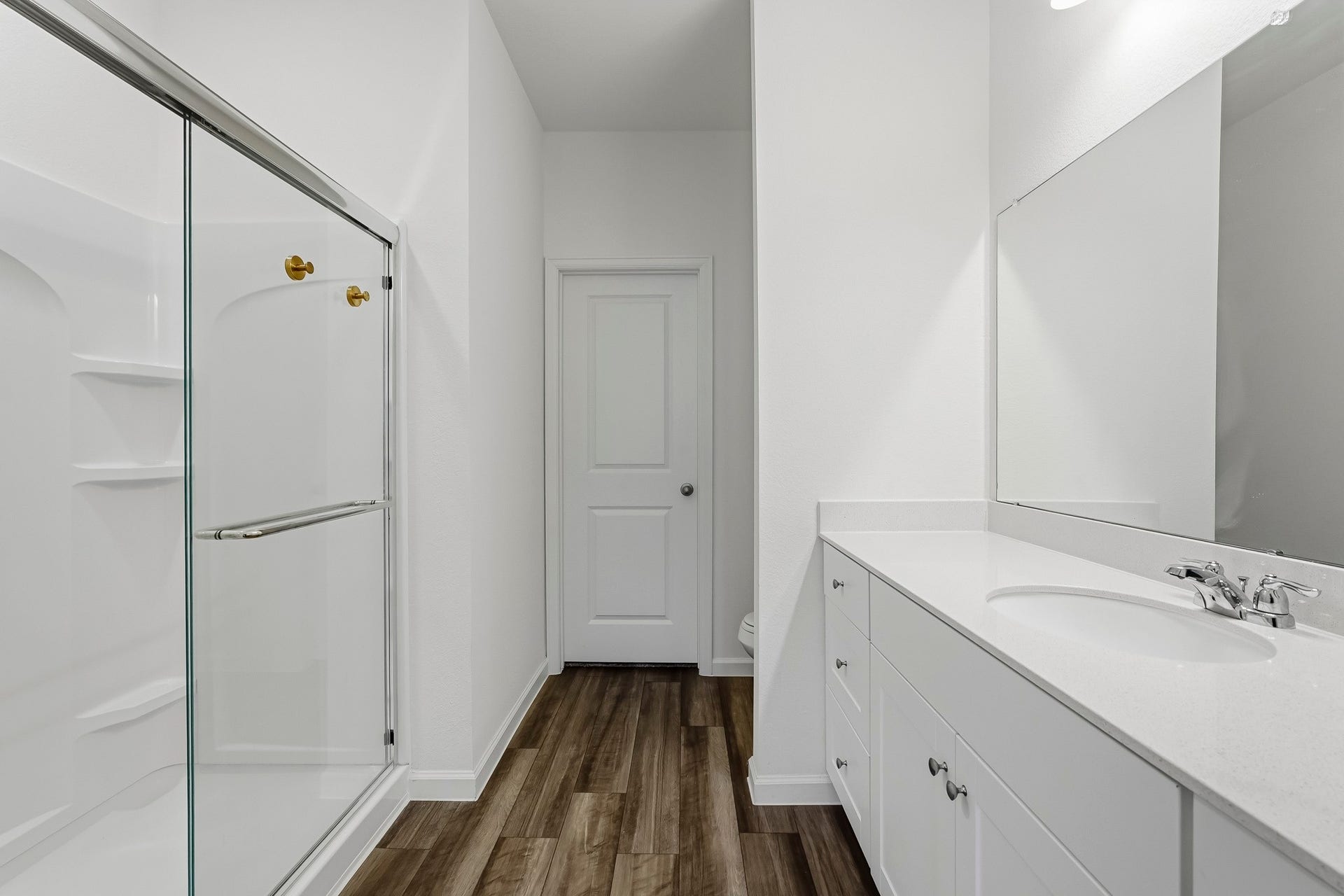 21547 Rolling Streams Drive, New Caney, TX 77357 This bright and spacious primary ensuite bathroom features a clean, modern design with crisp white walls, rich wood-look flooring, and elegant finishes throughout. At the back of the bathroom, a separate door leads to a walk-in closet, providing convenient storage and easy access to wardrobe essentials.