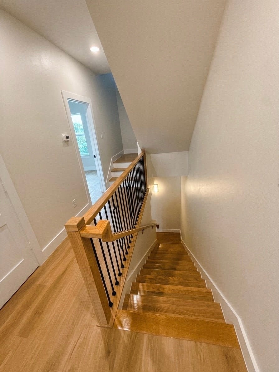 102 Sylvester Road, #C, Houston, TX 77009 Elegant wooden staircase with sleek black railing, leading to a bright upper hallway with crisp white walls and modern lighting.