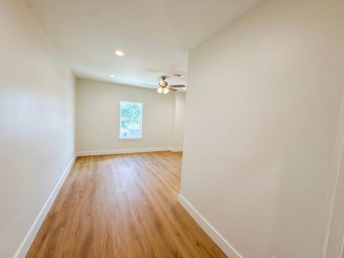 102 Sylvester Road, #C, Houston, TX 77009 Bright and spacious room with warm engineered wood flooring, recessed lighting, and a ceiling fan, offering a cozy atmosphere. A large window provides ample natural light.