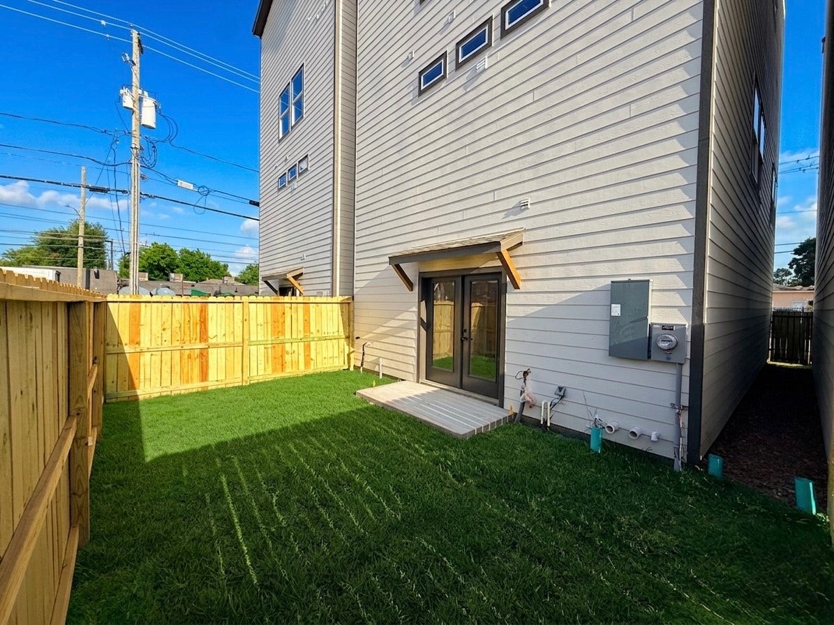 102 Sylvester Road, #C, Houston, TX 77009 Charming backyard with lush green grass, privacy fencing, and convenient access through elegant double doors, perfect for outdoor relaxation and entertainment.