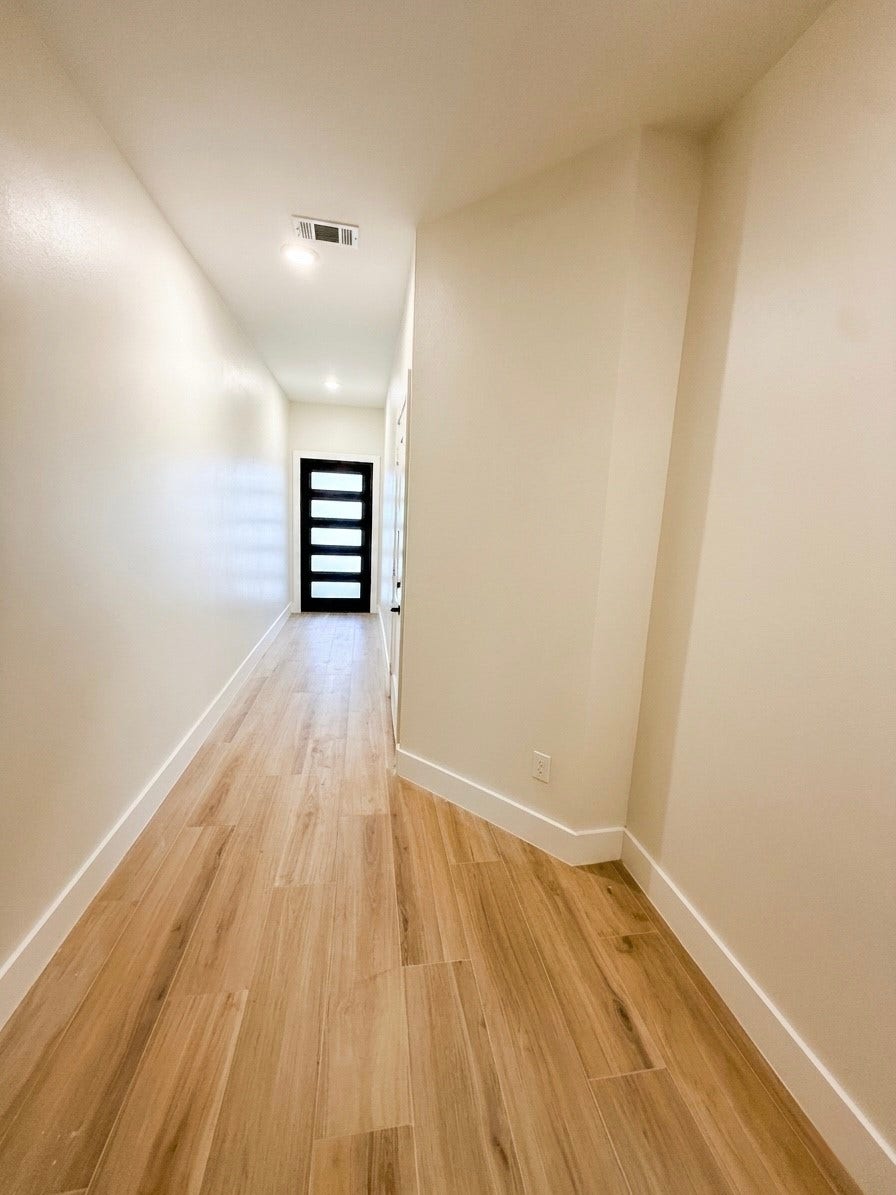 102 Sylvester Road, #C, Houston, TX 77009 A sleek, modern hallway with light porcelain flooring and a contemporary door at the end, offering a warm and inviting entrance.