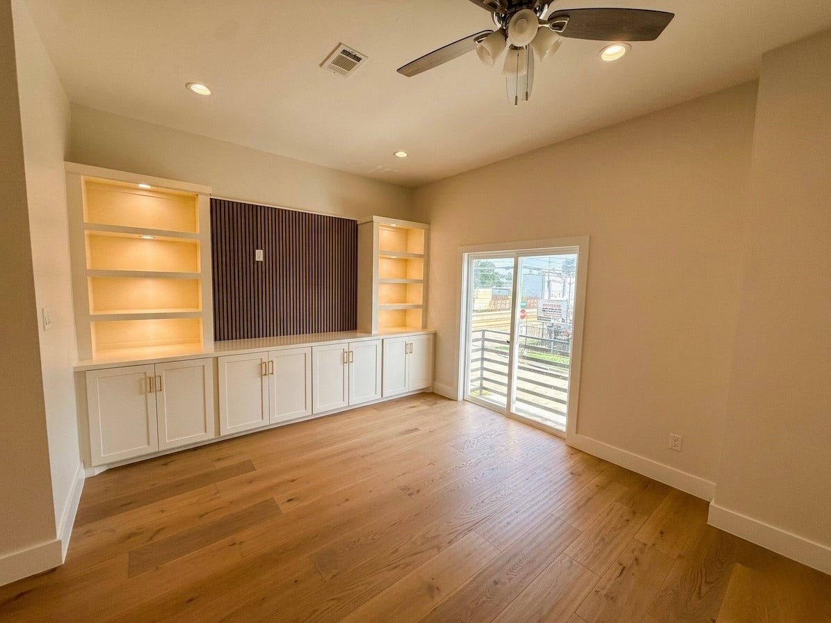102 Sylvester Road, #C, Houston, TX 77009 Bright, spacious room featuring built-in illuminated shelving, elegant cabinetry, and a large sliding glass door leading to an outdoor view.