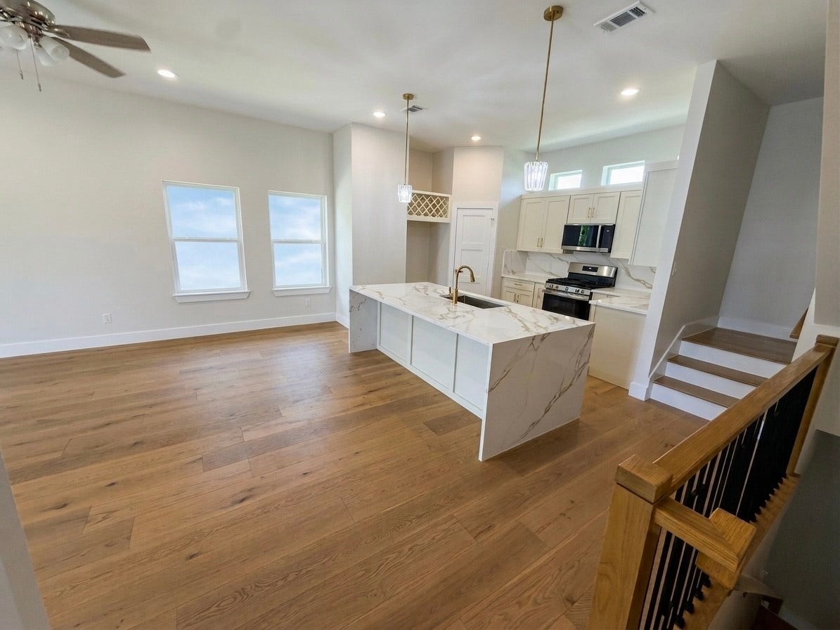 102 Sylvester Road, #C, Houston, TX 77009 Bright and open kitchen with a large quarts island, elegant pendant lighting, and modern stainless steel appliances, seamlessly flowing into a spacious living area with hardwood engineered floors.