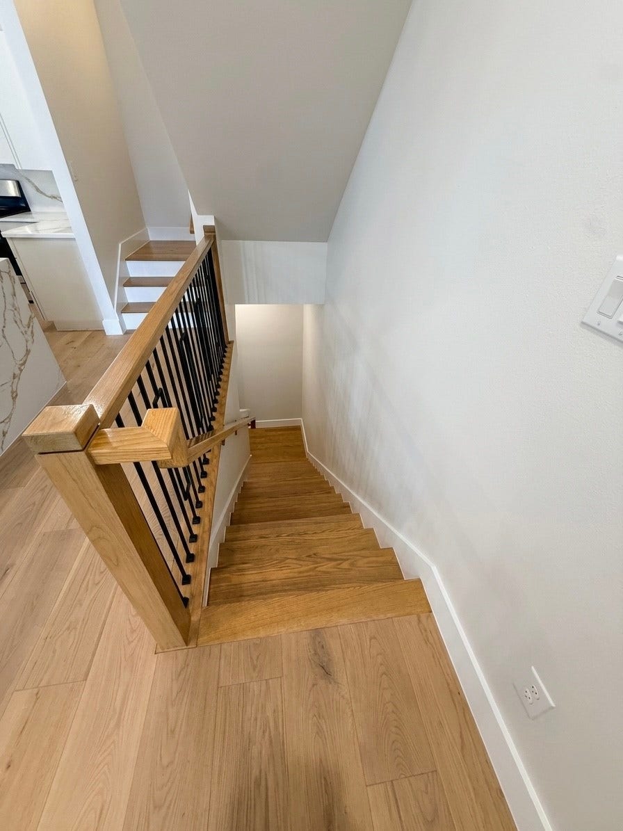 102 Sylvester Road, #C, Houston, TX 77009 Elegant wooden staircase with sleek black railings, leading down from a bright, open space with light wood flooring.