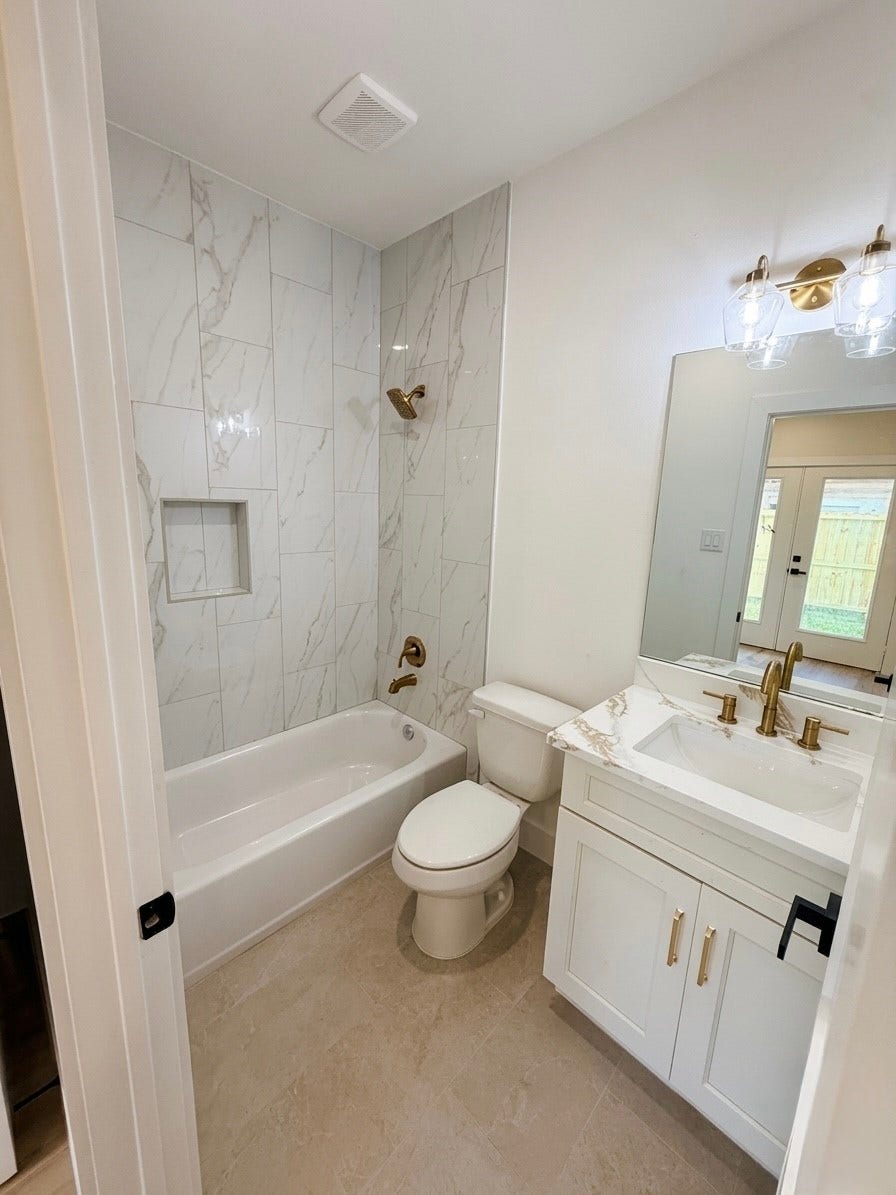 102 Sylvester Road, #C, Houston, TX 77009 Elegant bathroom 1st floor featuring a modern tub with marble-style tile, chic brass fixtures, and a stylish vanity with ample lighting.