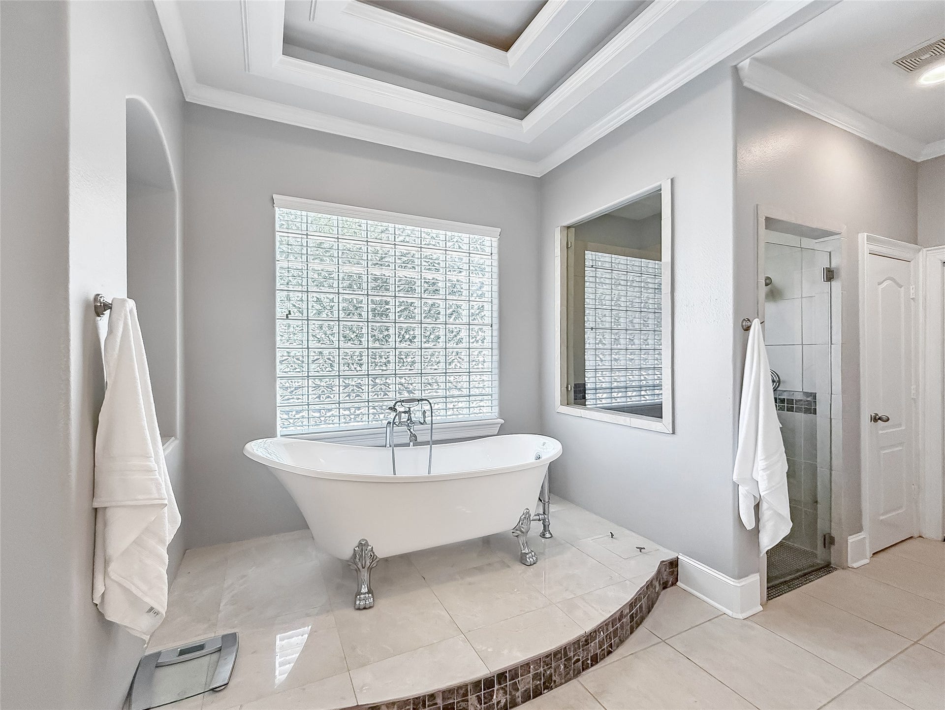 7611 Kings River Lane, Humble, TX 77346 Primary bath retreat centers around a freestanding clawfoot tub positioned beneath a large glass-block window, complemented by architectural ceiling details and a separate shower area.