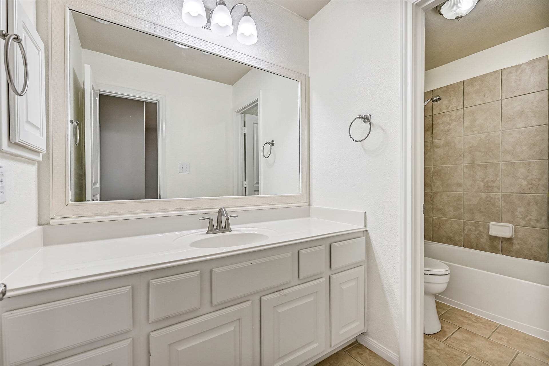 2508 Rockygate Lane, Friendswood, TX 77546 This Jack & Jill style bathroom serves the adjoining secondary bedrooms and is thoughtfully designed with separate vanity and bathing areas for added functionality. Features include a lengthy cultured marble countertop with an undermount basin sink, a seated makeup vanity with lap drawer, white cabinetry, updated lighting, tile floors, and a private combination bathtub and shower with a tile surround.