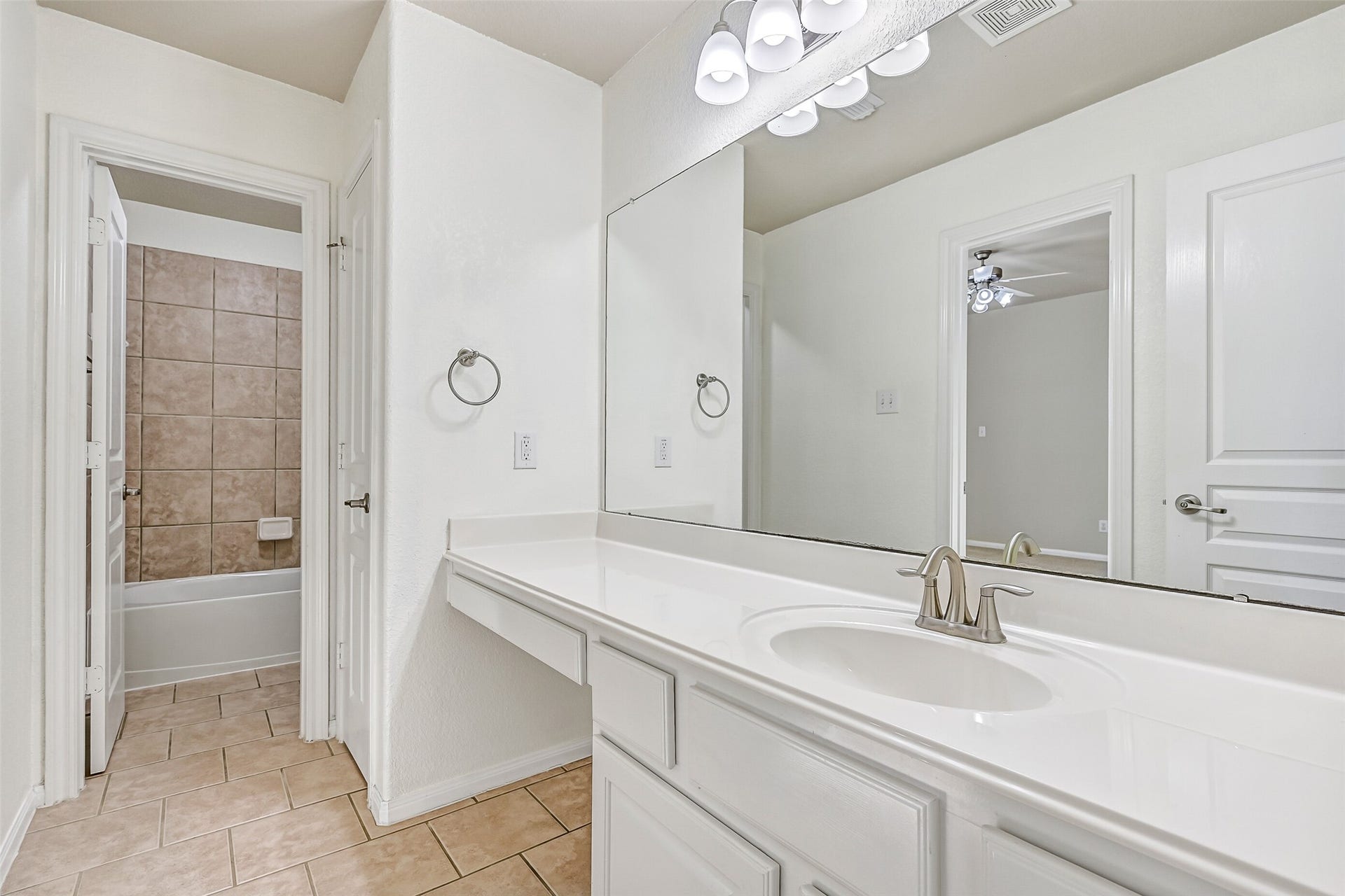 2508 Rockygate Lane, Friendswood, TX 77546 This Jack & Jill style bathroom serves the adjoining secondary bedrooms and is thoughtfully designed with separate vanity and bathing areas for added functionality. Features include a lengthy cultured marble countertop with an undermount basin sink, a seated makeup vanity with lap drawer, white cabinetry, updated lighting, tile floors, and a private combination bathtub and shower with a tile surround.