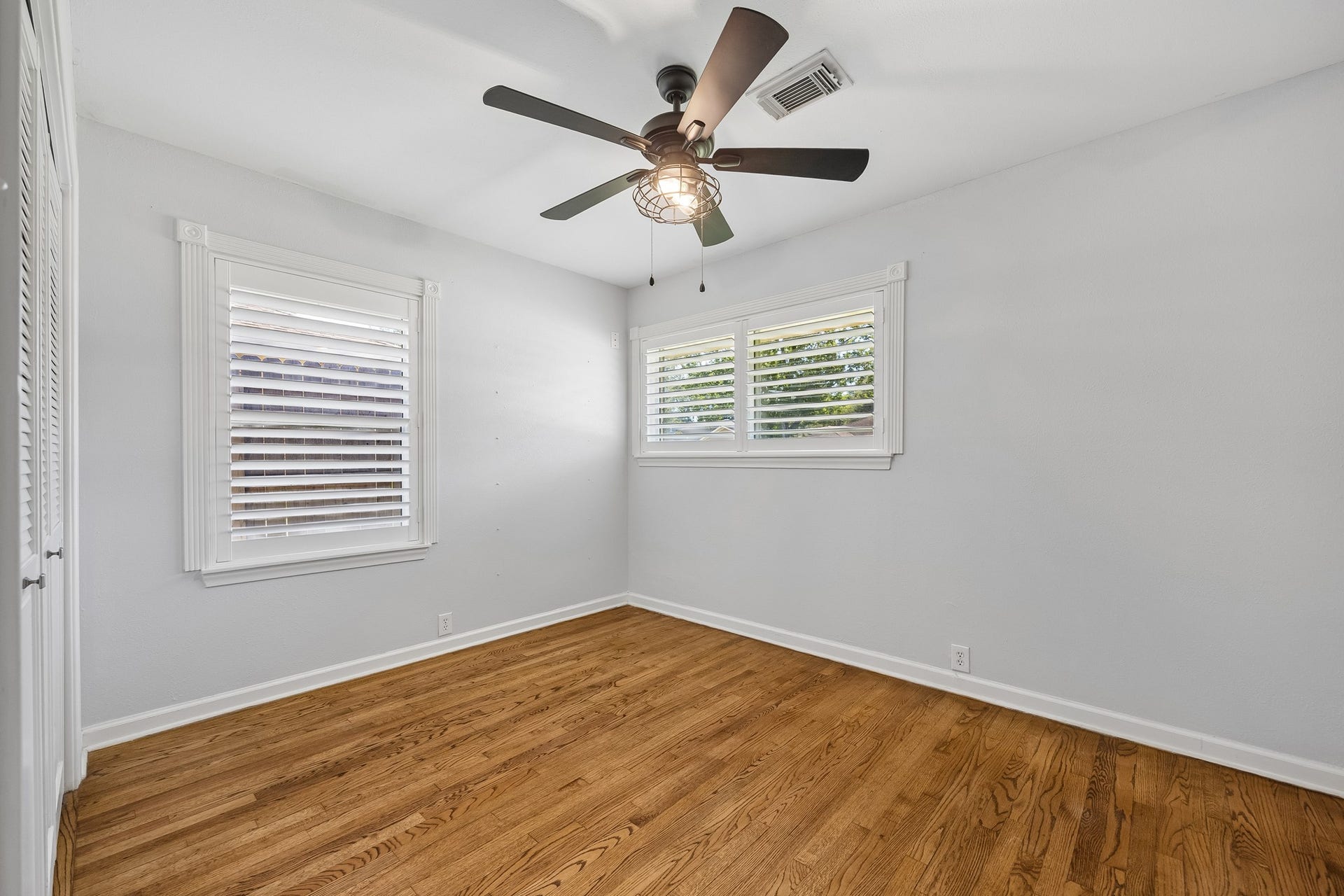 From a corner of the primary suite, this angle shows the connection to the ensuite bath, including the double-sink vanity and windows with plantation shutters that bring in natural light.