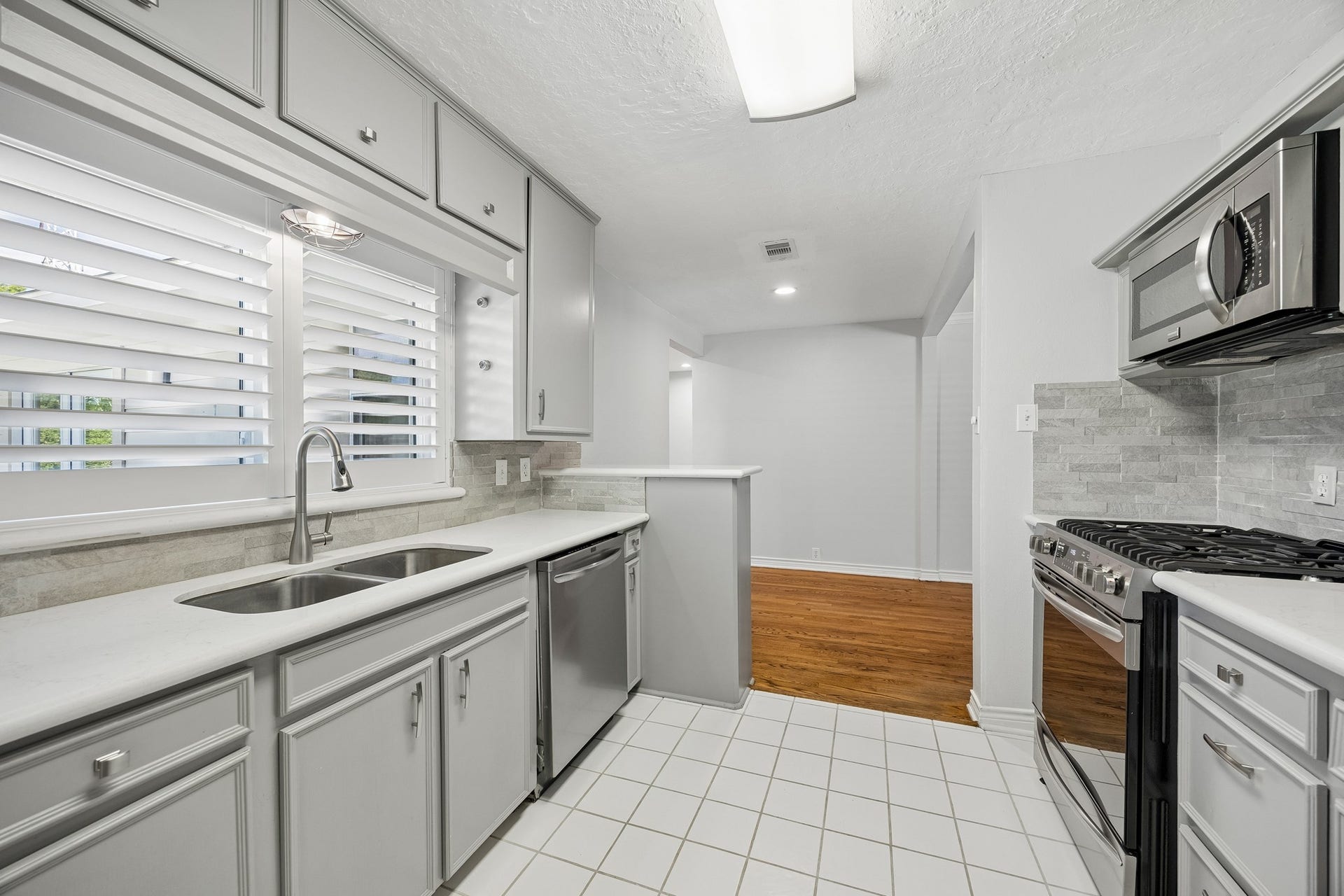 A wider view from the dining area shows how the living and dining spaces connect, with the front entry in sight and a glimpse into the kitchen, including additional storage beneath the bar area.