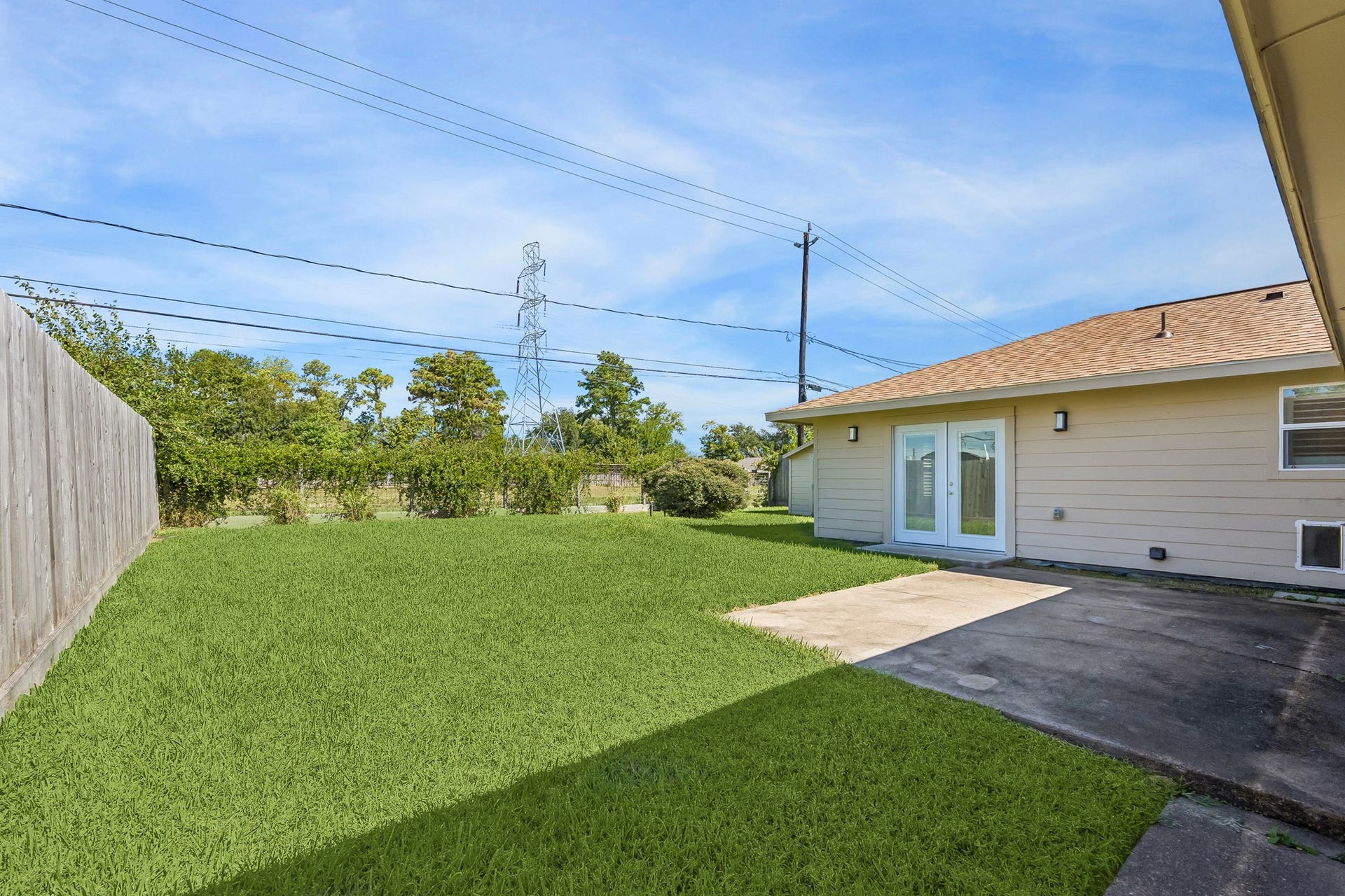A view from the far corner of the yard looking back toward the home, showcasing the expansive green space, rear patio slab, and French doors off the primary suite that open directly to the backyard.