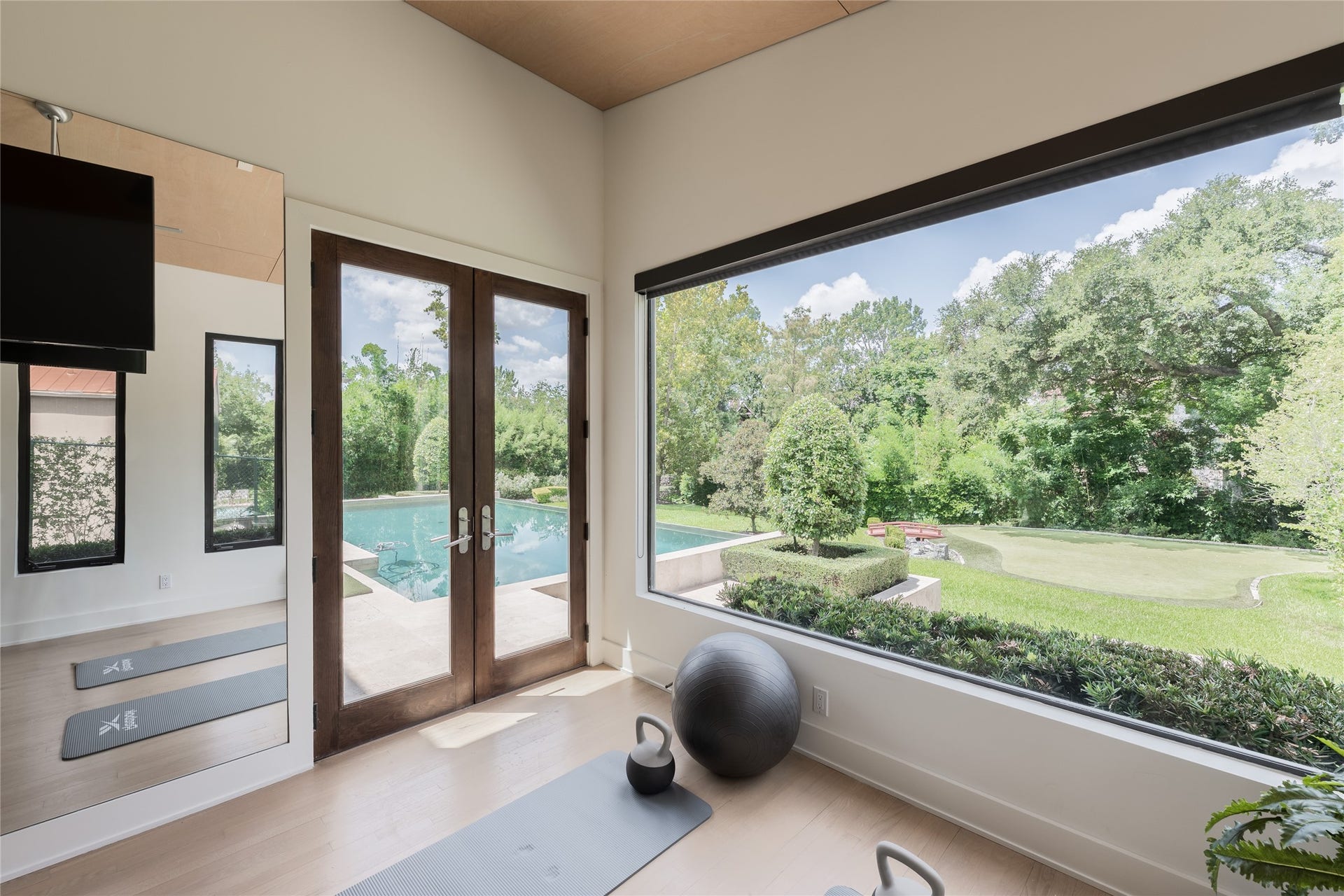 309 Glenwood Drive, Houston, TX 77007 A second perspective of the wellness studio highlights its connection to the grounds, with oversized windows capturing views of the pool, putting green and mature landscaping. Glass doors provide direct outdoor access, extending the space naturally into the backyard.