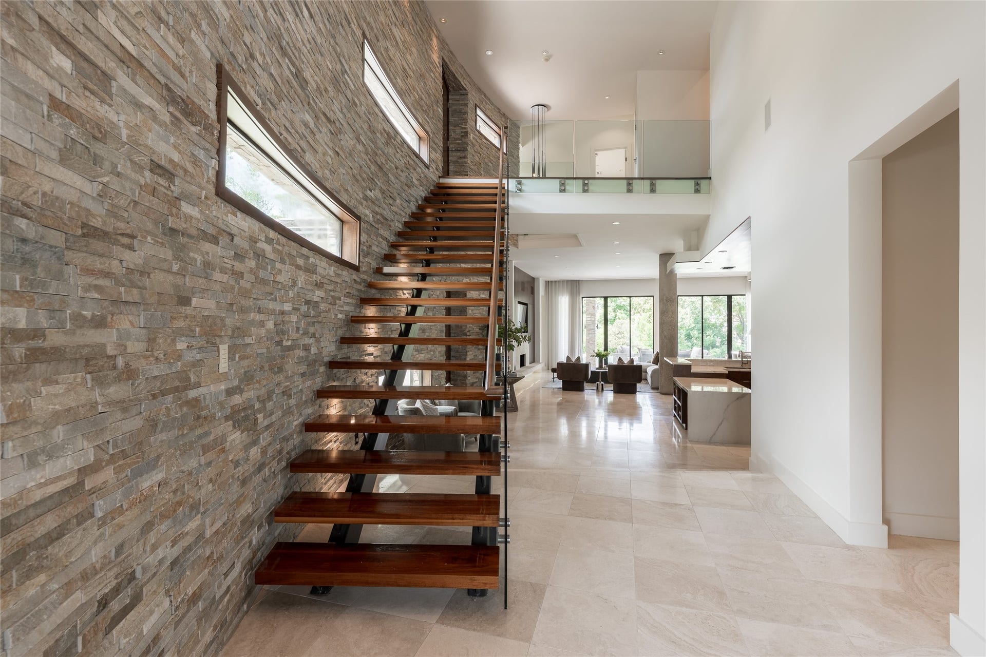 309 Glenwood Drive, Houston, TX 77007 The homes signature curved stacked-stone wall continues along the staircase, creating a strong architectural feature between levels. Floating walnut stair treads extend from the stone with an open-riser design, pairing two of the homes defining natural materials in one sculptural element.