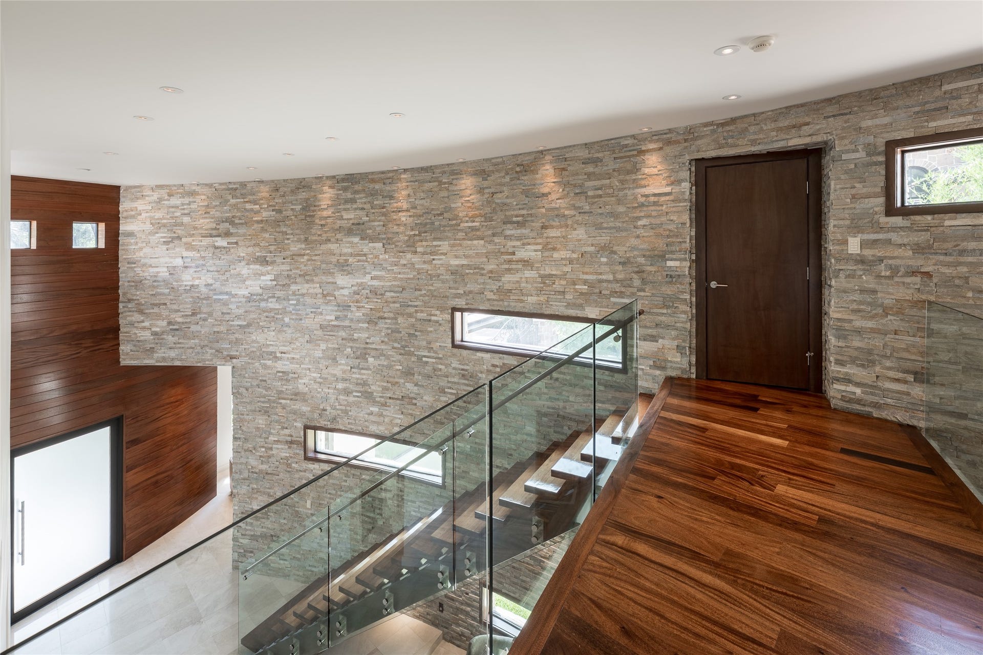 309 Glenwood Drive, Houston, TX 77007 The upstairs landing continues the homes curved stacked-stone wall and walnut flooring, overlooking the floating staircase below. A dedicated storage closet is integrated along the landing, adding practical storage without interrupting the open architectural design.