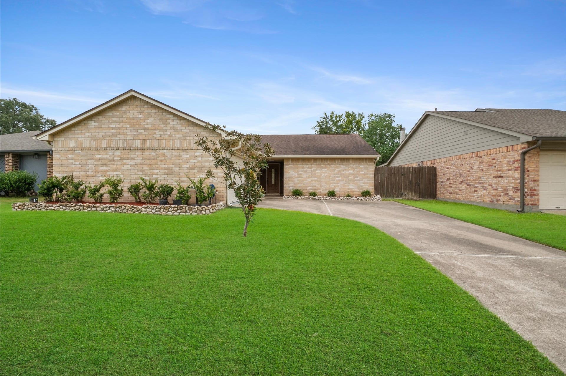 15414 Evergreen Place Drive Drive, Houston, TX 77083 Well-maintained single-story brick home featuring a spacious driveway, attached garage, manicured lawn, and neatly landscaped flower beds.