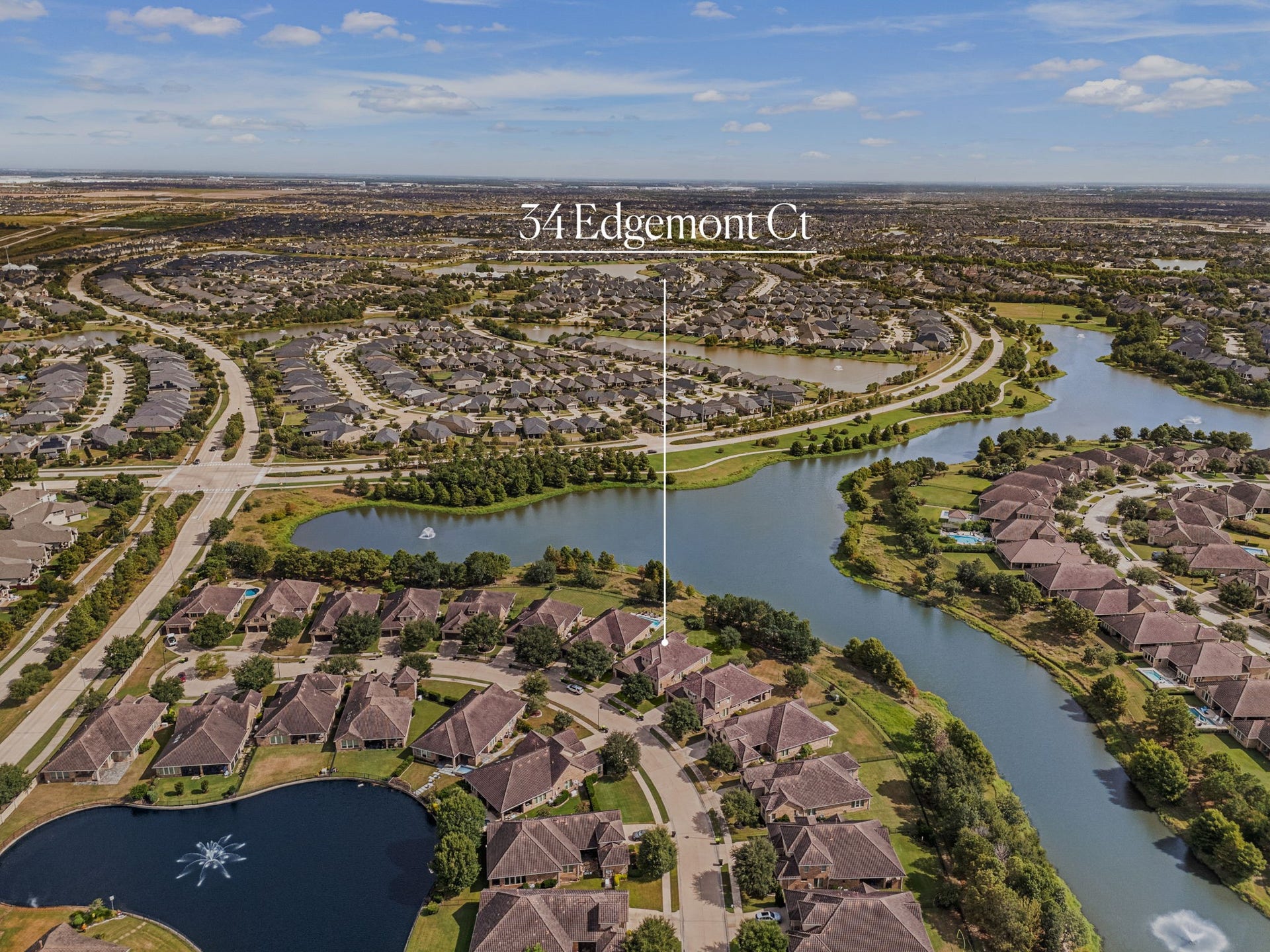 34 Edgemont Court, Fulshear, TX 77441 This aerial view highlights the home's prime setting along the community's scenic lake, with tree-lined streets and gated access throughout the neighborhood.