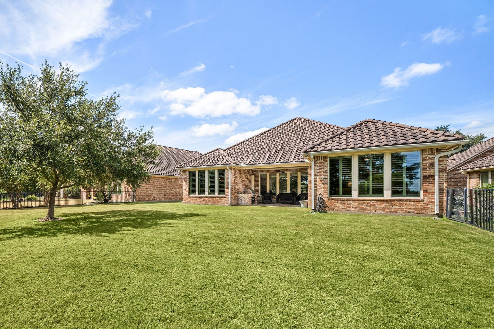 34 Edgemont Court, Fulshear, TX 77441 A sprawling backyard offers plenty of room to relax or entertain, shaded by mature trees and enclosed by a wrought iron fence.
