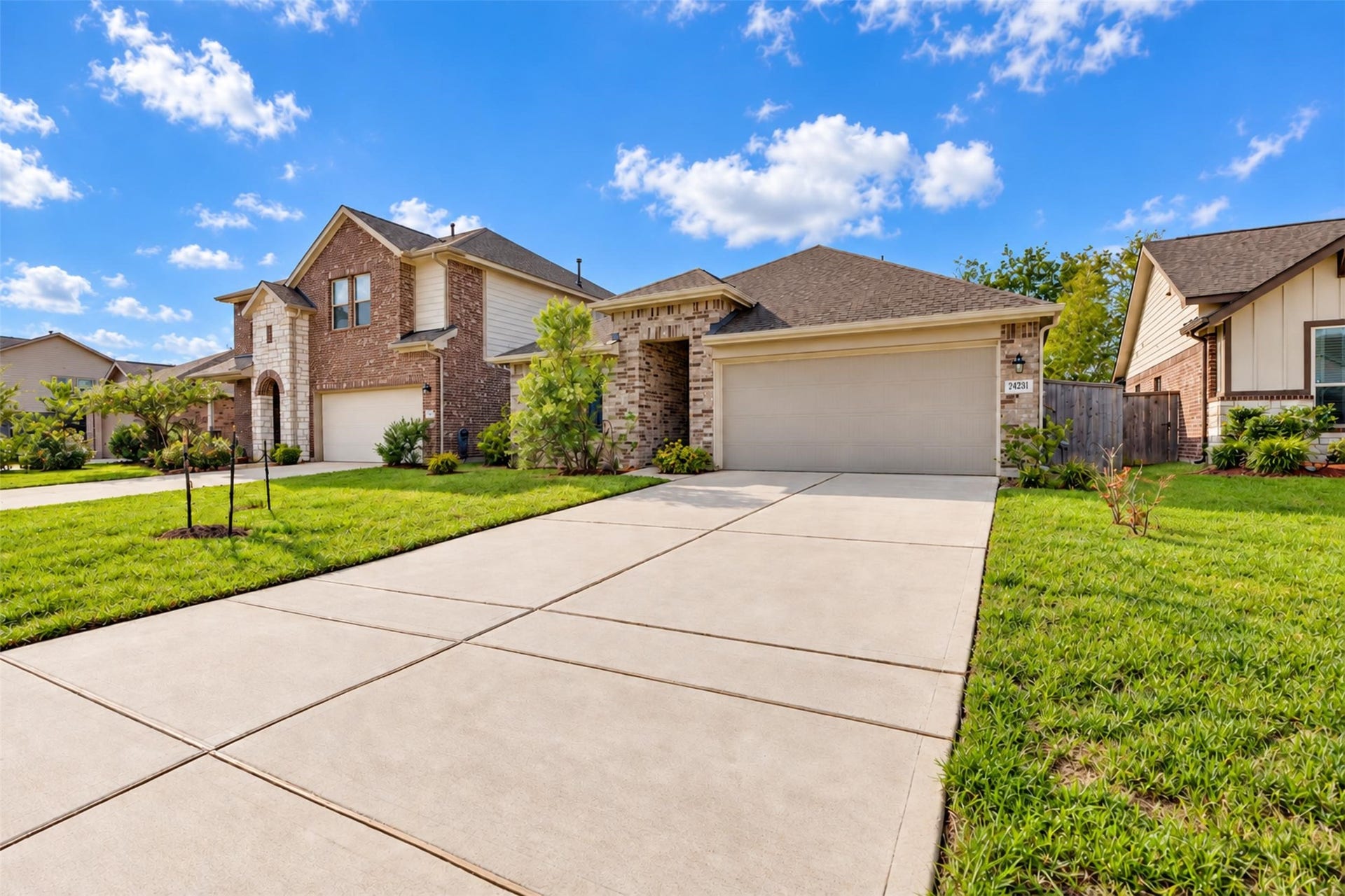 Front view featuring a spacious driveway, two-car garage, attractive brick exterior, and well-maintained landscaping.