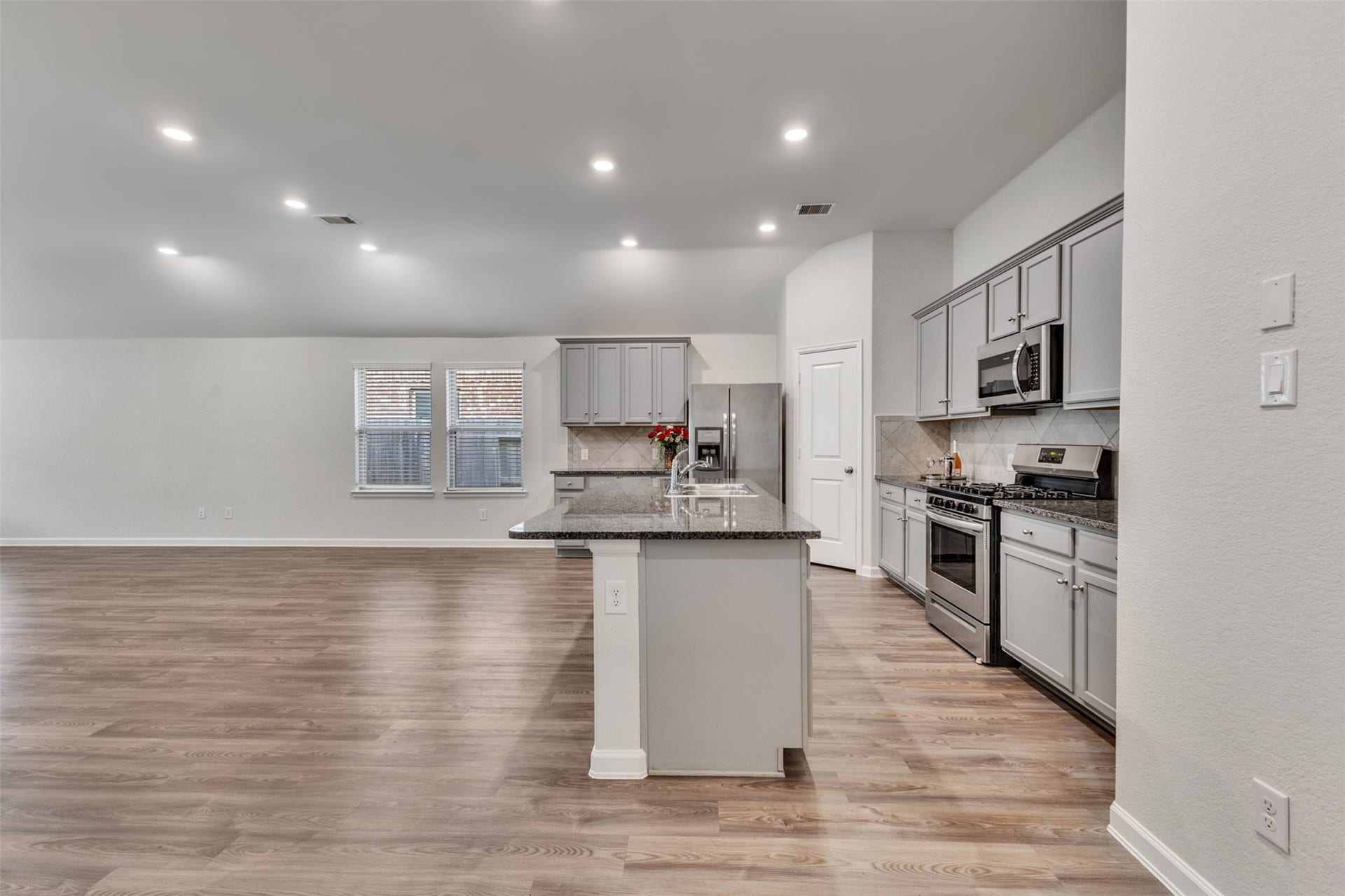 Open-concept kitchen and living area featuring granite countertops, stainless steel appliances, abundant cabinetry, vinyl plank flooring, and recessed lighting.
