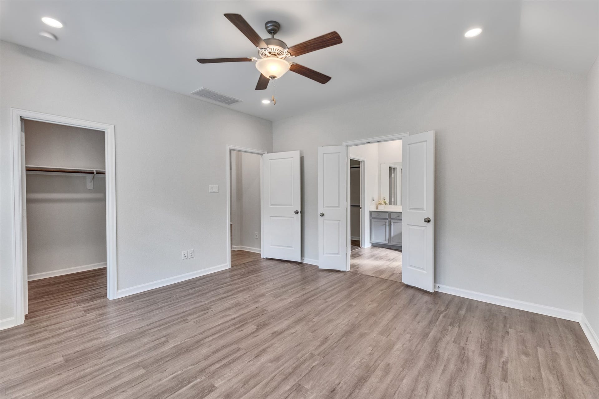 Spacious primary bedroom featuring vinyl plank flooring, ceiling fan, recessed lighting, and direct access to the primary bathroom and walk-in closet.