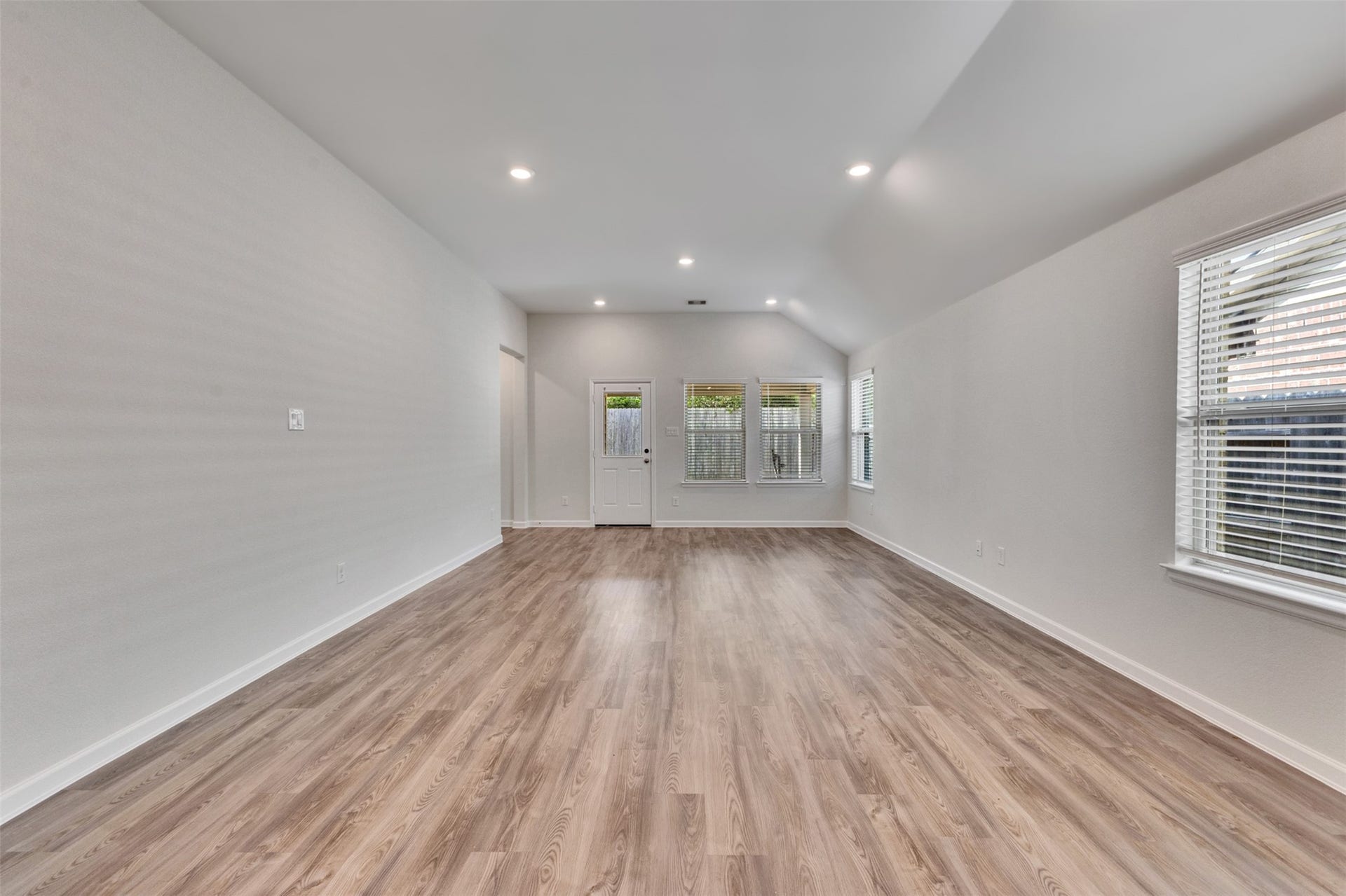 Spacious open living area featuring high ceilings, recessed lighting, vinyl plank flooring, and abundant natural light.