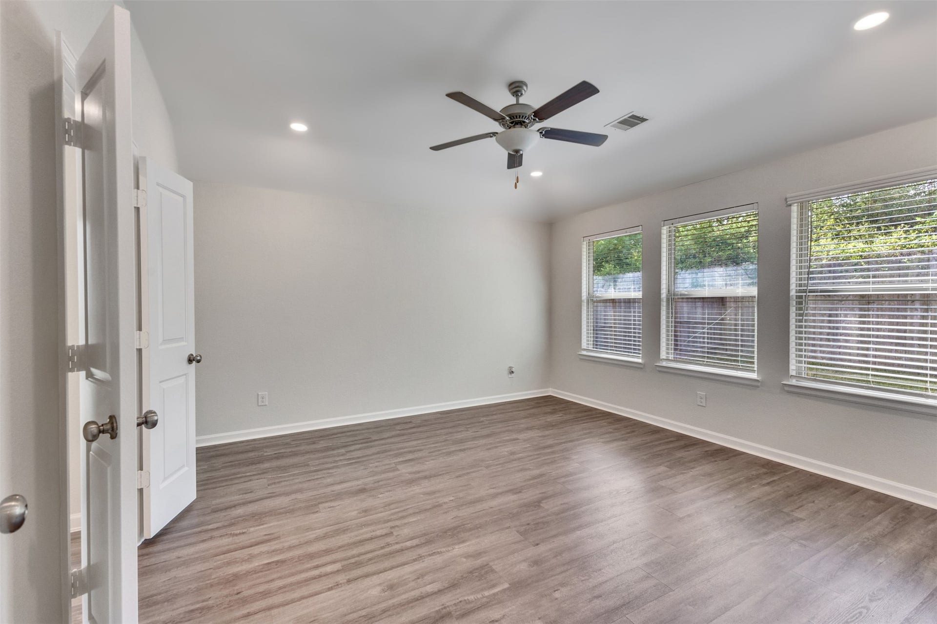 Spacious primary bedroom featuring vinyl plank flooring, ceiling fan, recessed lighting, and abundant natural light.