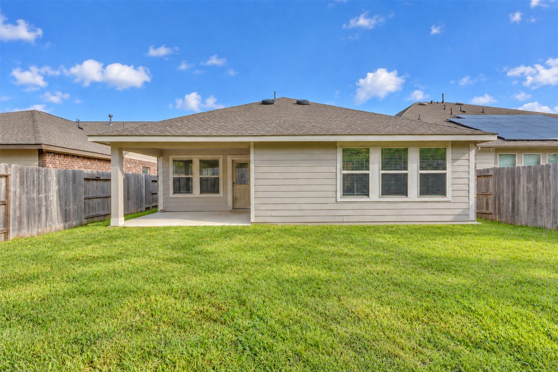 Rear exterior view showcasing a spacious fully fenced backyard and covered patio.