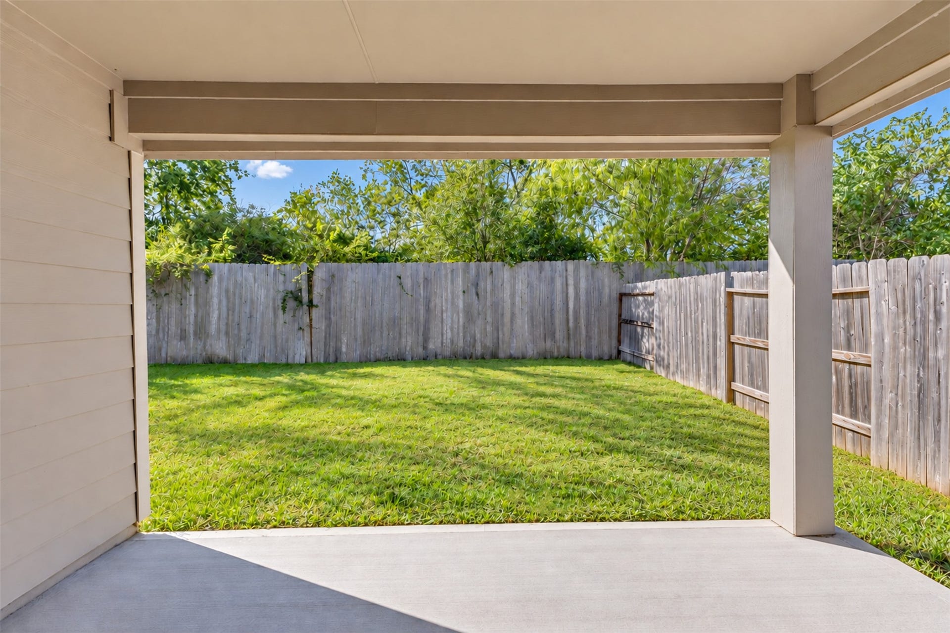 Covered back patio overlooking a spacious, fully fenced backyard with mature greenery.