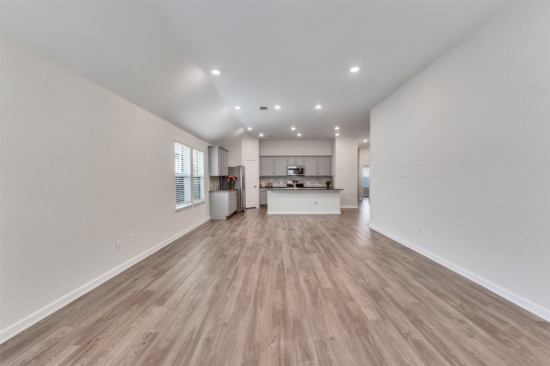 Spacious open-concept living area featuring vinyl plank flooring, high ceilings, recessed lighting, and a seamless flow into the kitchen.