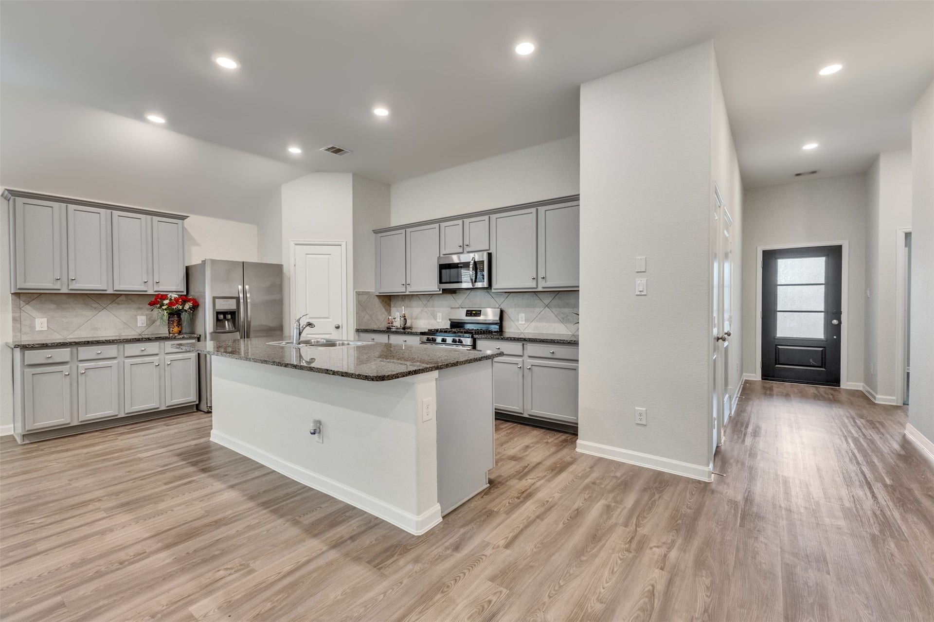 Kitchen featuring a large granite island, abundant cabinetry, stainless steel appliances, recessed lighting, and an open view toward the entry foyer.