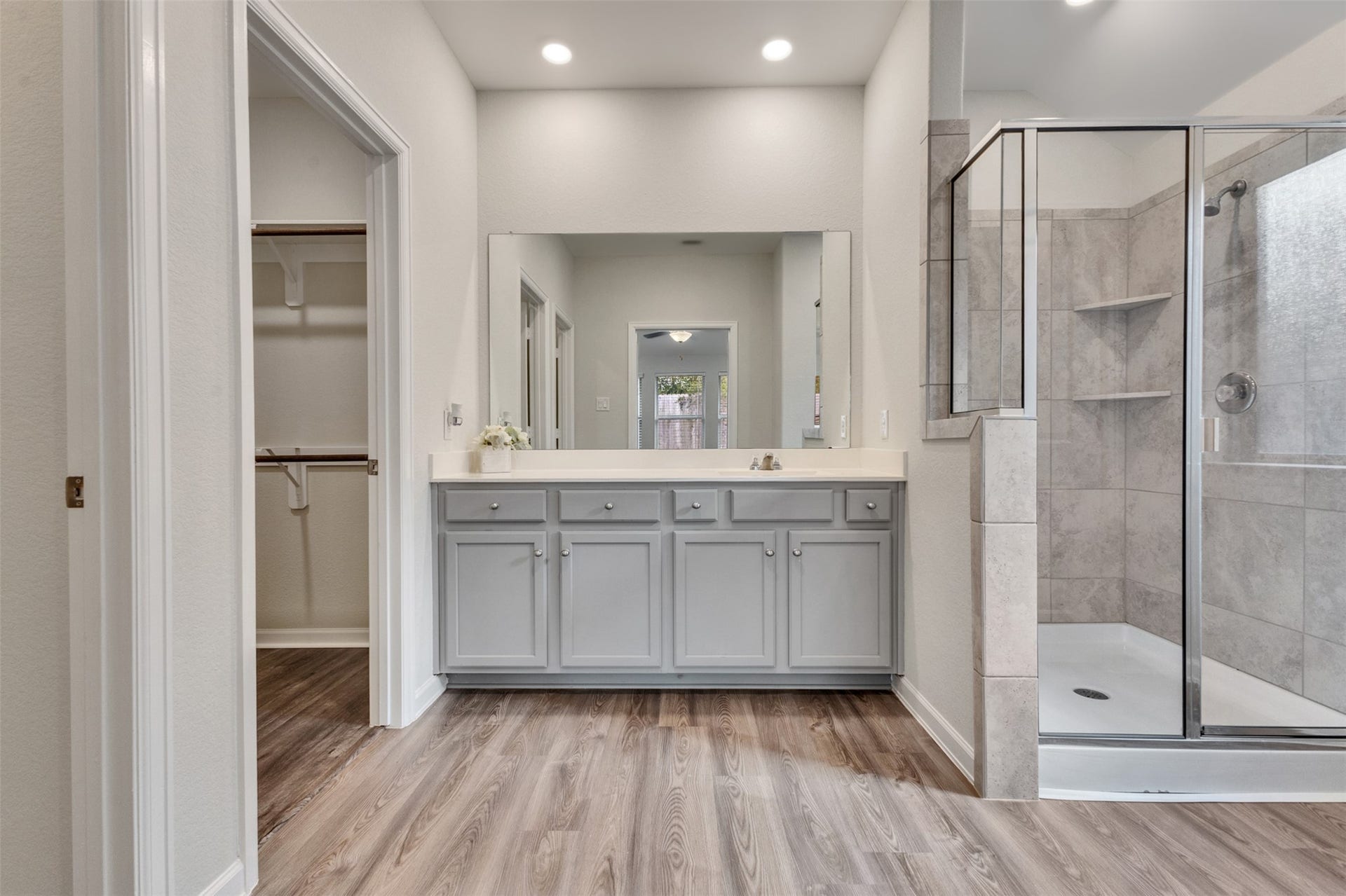 Primary bathroom featuring a spacious vanity, tiled walk-in shower with glass enclosure, recessed lighting, and walk-in closet.