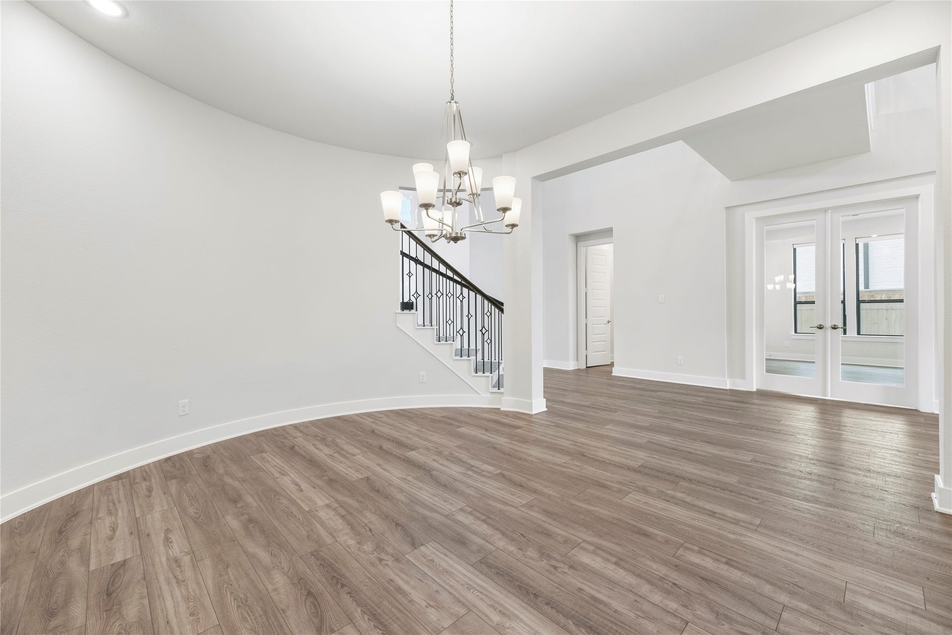 View from the dining area highlighting the seamless open layout, statement chandelier, main staircase, and access to adjacent living spaces.