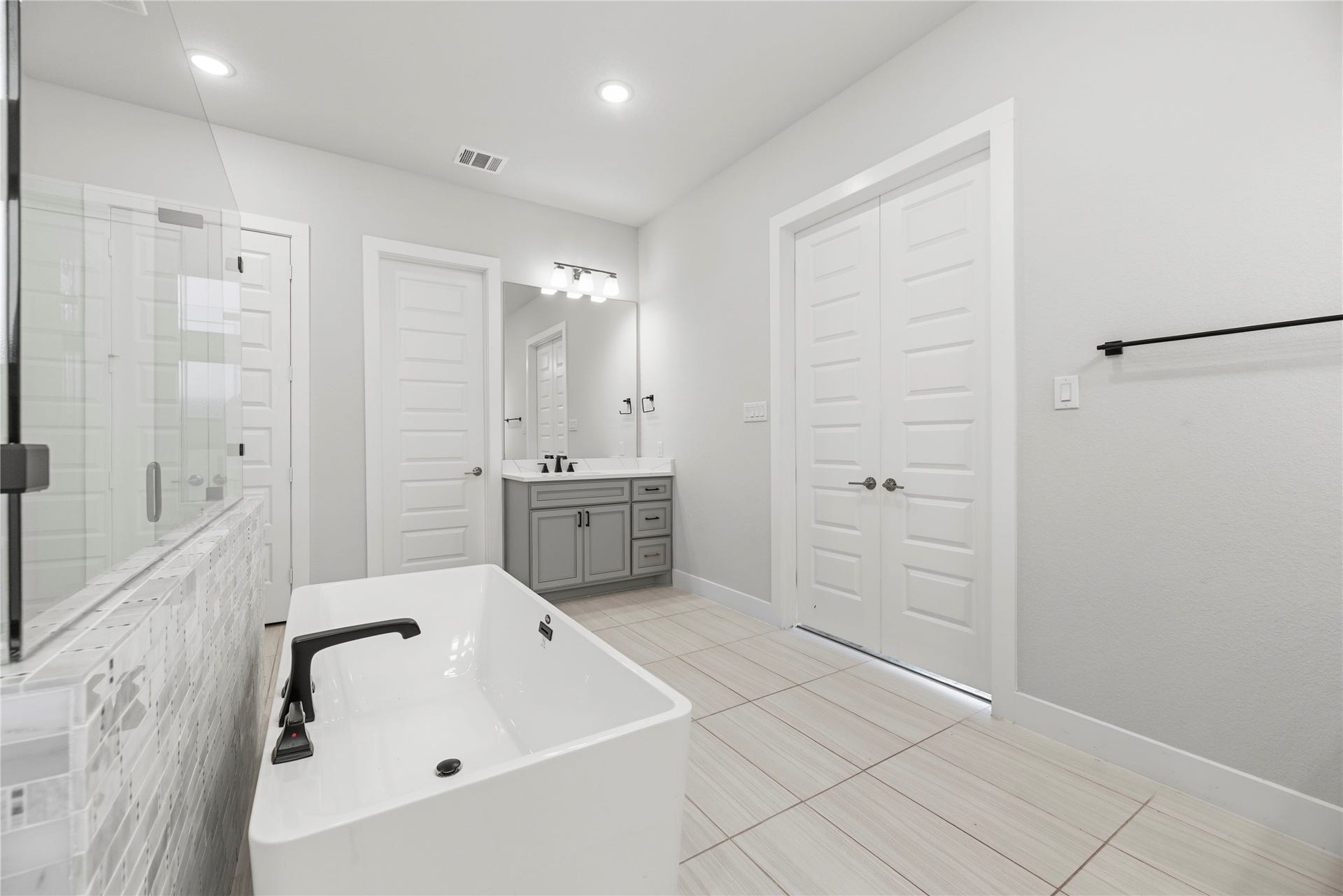 Spacious layout overview showing double-door bedroom entry, grey shaker cabinetry with quartz countertops, matte black hardware, and bright recessed lighting.