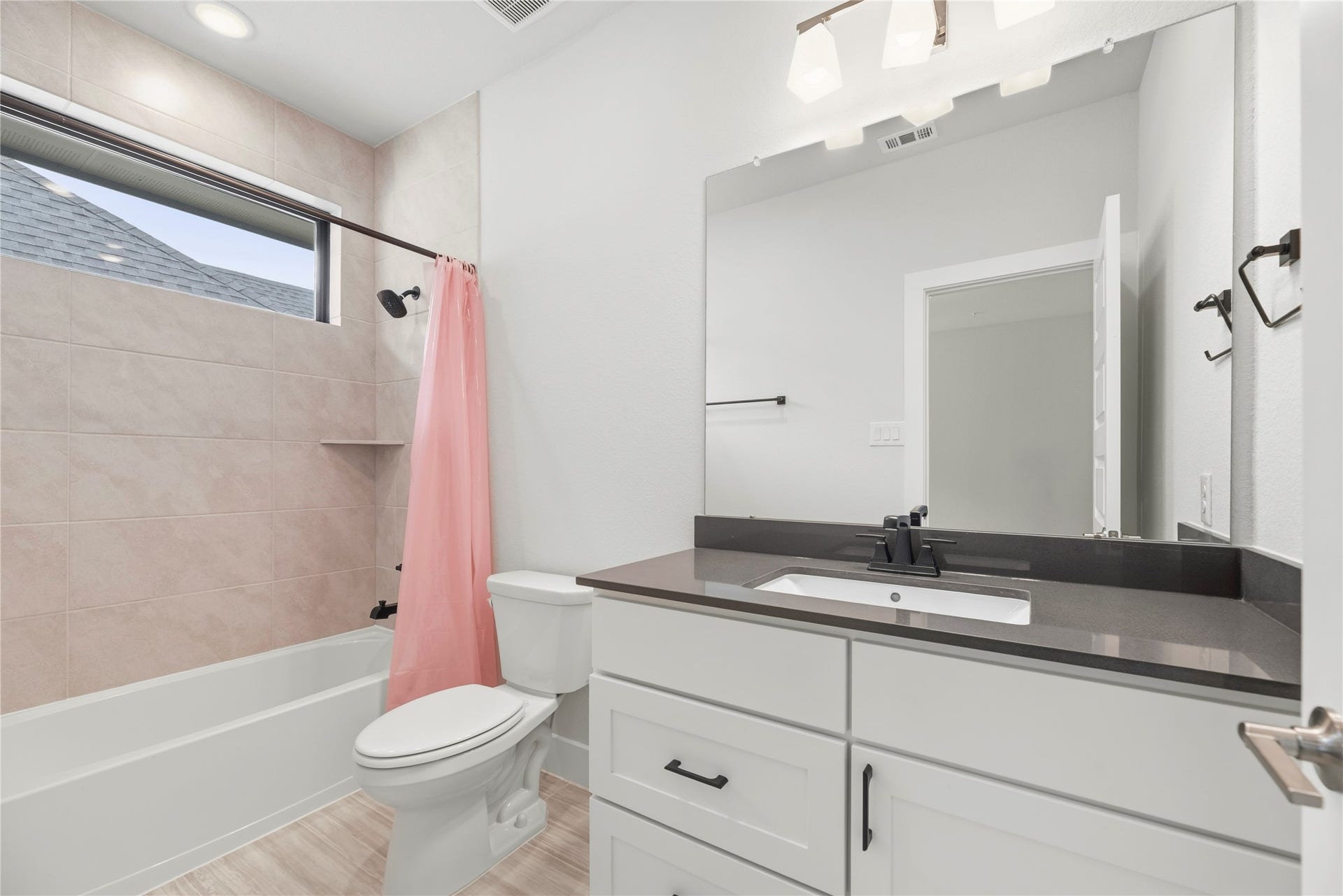 Stylish bathroom offering dark quartz vanity tops, white cabinetry, modern matte black fixtures, and a high transom window for natural light and privacy.