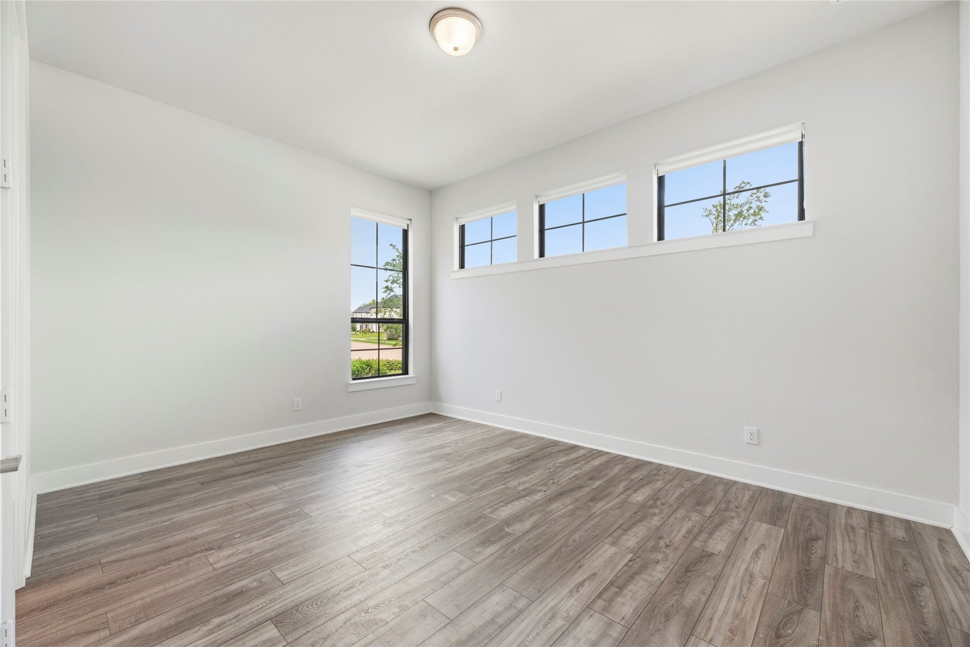 Versatile main-level bedroom featuring wood-look vinyl plank flooring, neutral paint, and high transom windows for elevated natural light and privacy.