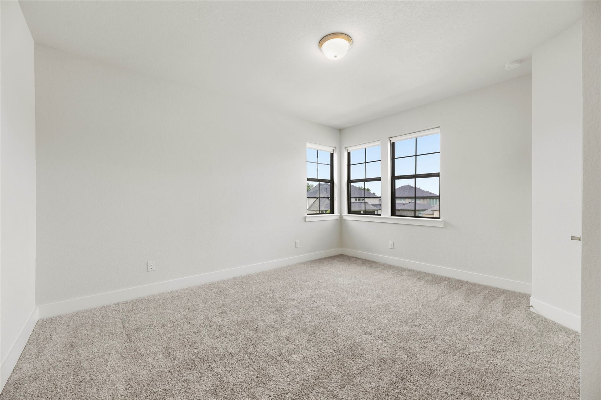 Light-filled guest room featuring cozy plush carpeting, clean white trim, and corner windows bringing in abundant natural light.