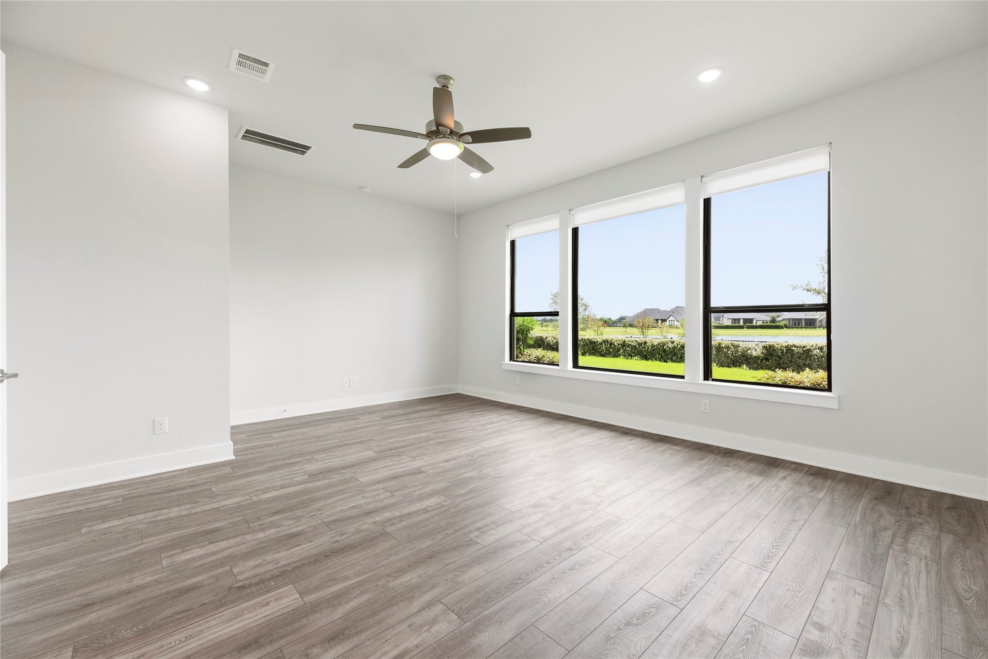 Bright and spacious primary bedroom featuring wall-to-wall wood-look flooring, ceiling fan, and large picture windows framing serene lake views.
