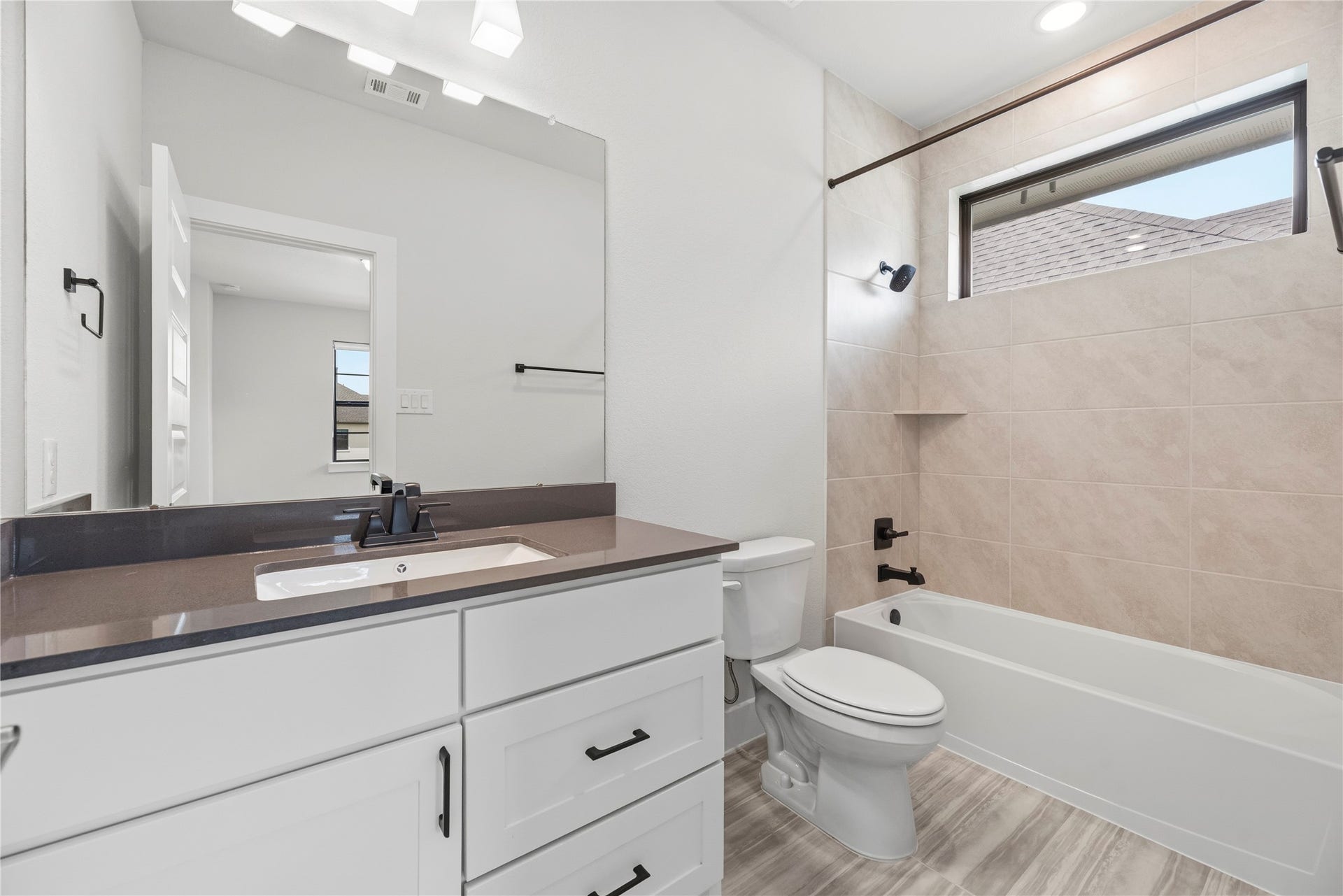Clean and contemporary bathroom complete with dark quartz countertops, modern black fixtures, and custom tilework extending to the ceiling around the tub.