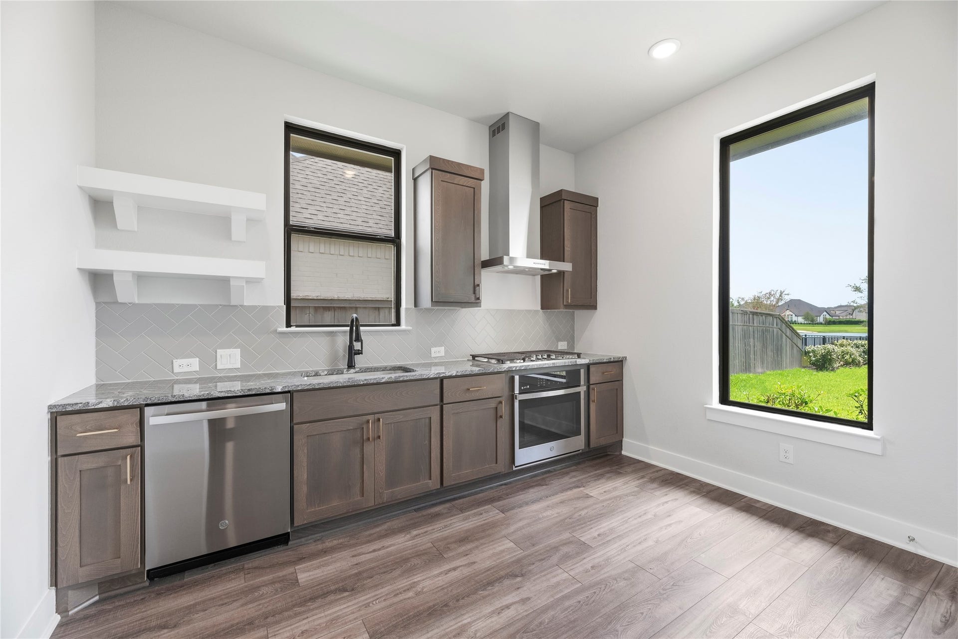 Well-appointed private secondary kitchen featuring rich wood shaker cabinetry, granite countertops, stainless steel appliances with gas cooktop and dishwasher, open shelving, and a large picture window overlooking the yard.