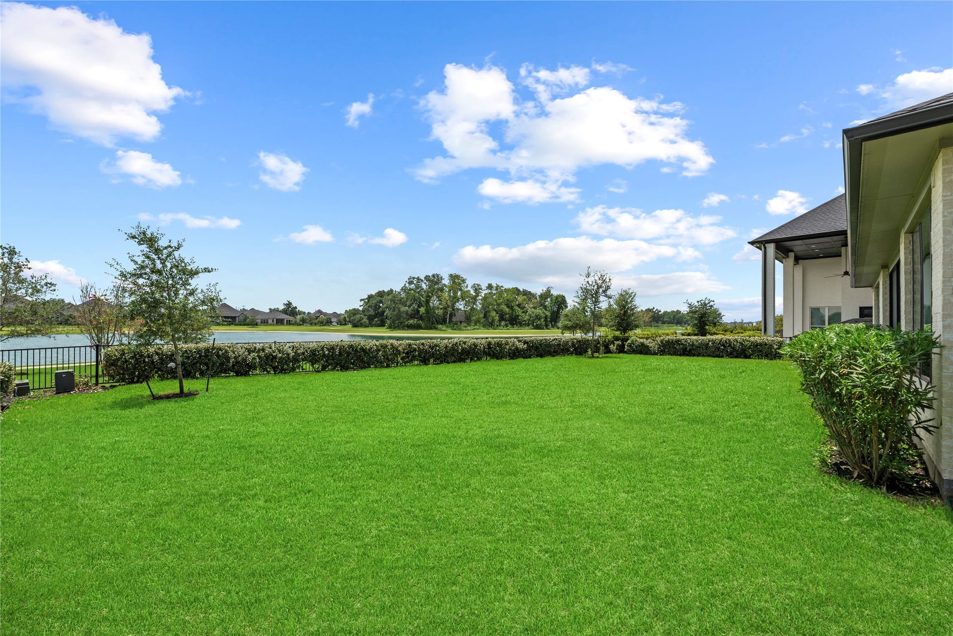 Bright and open side-yard angle highlighting the lush turf, low-maintenance landscaping, and scenic lake backdrop.