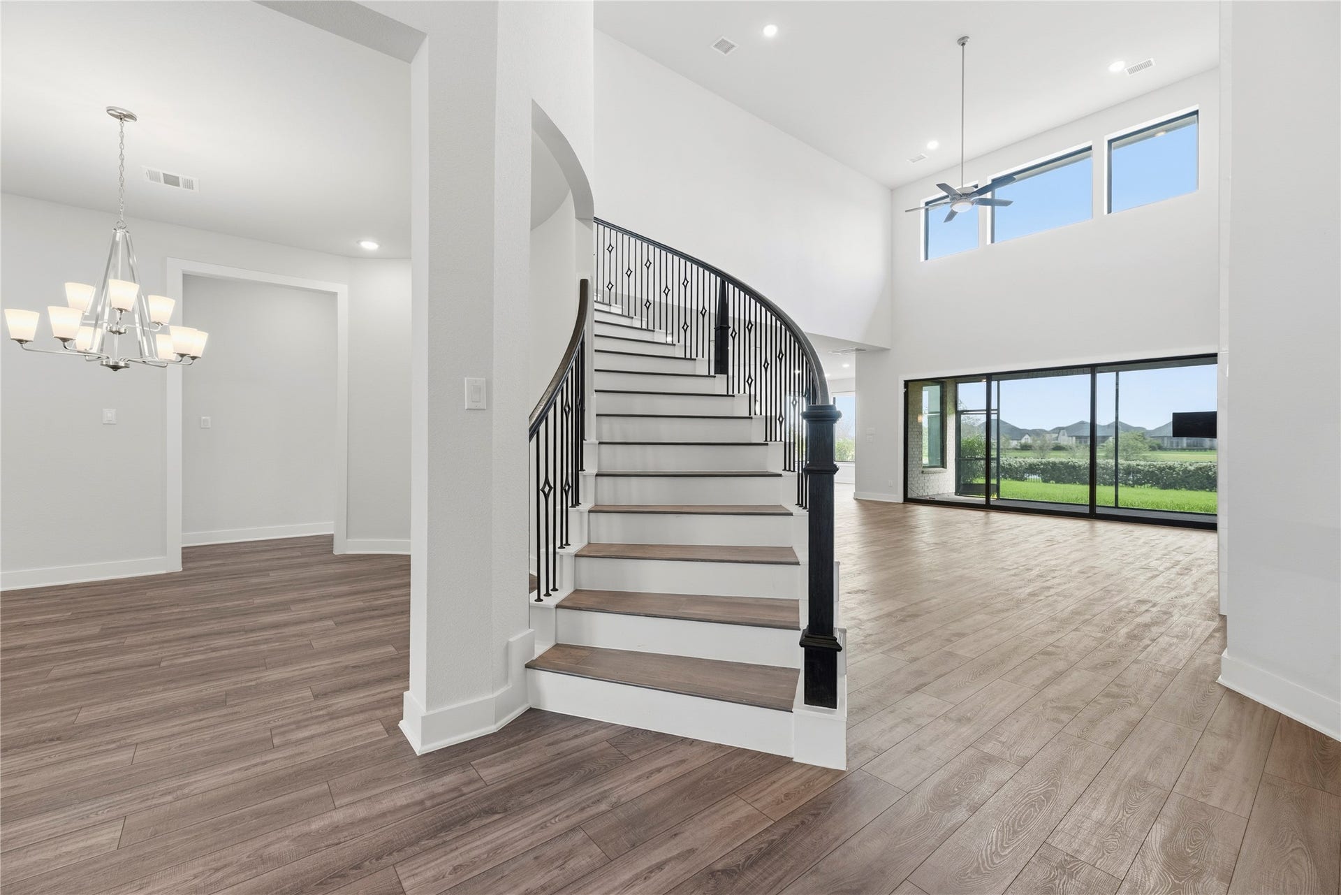 Architectural focal point featuring a grand curved staircase with iron spindles, flowing directly into a two-story great room with massive glass patio sliders.