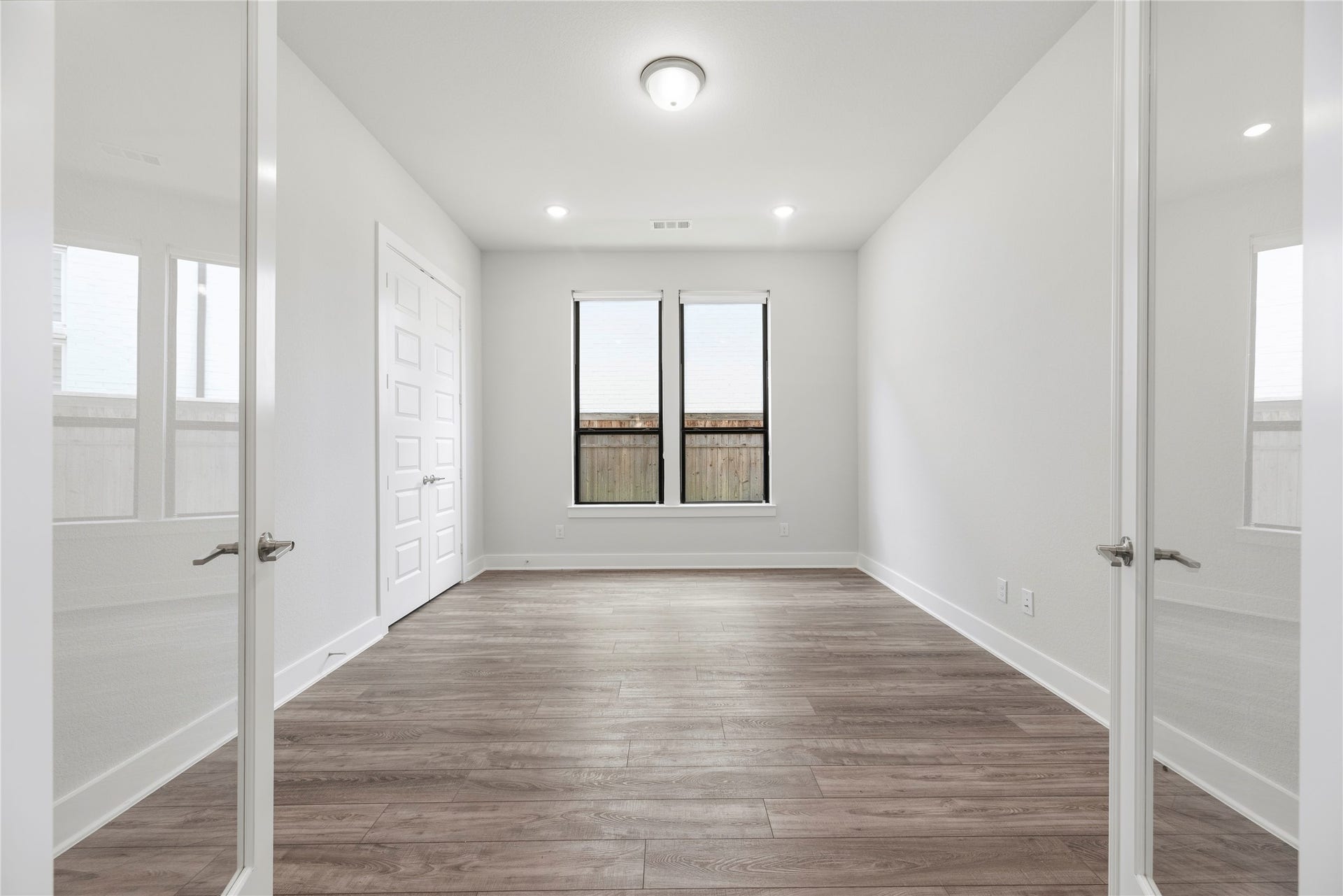 Dedicated main-floor office framed by elegant double French doors, featuring wood-look flooring, recessed lighting, and rear-facing windows.