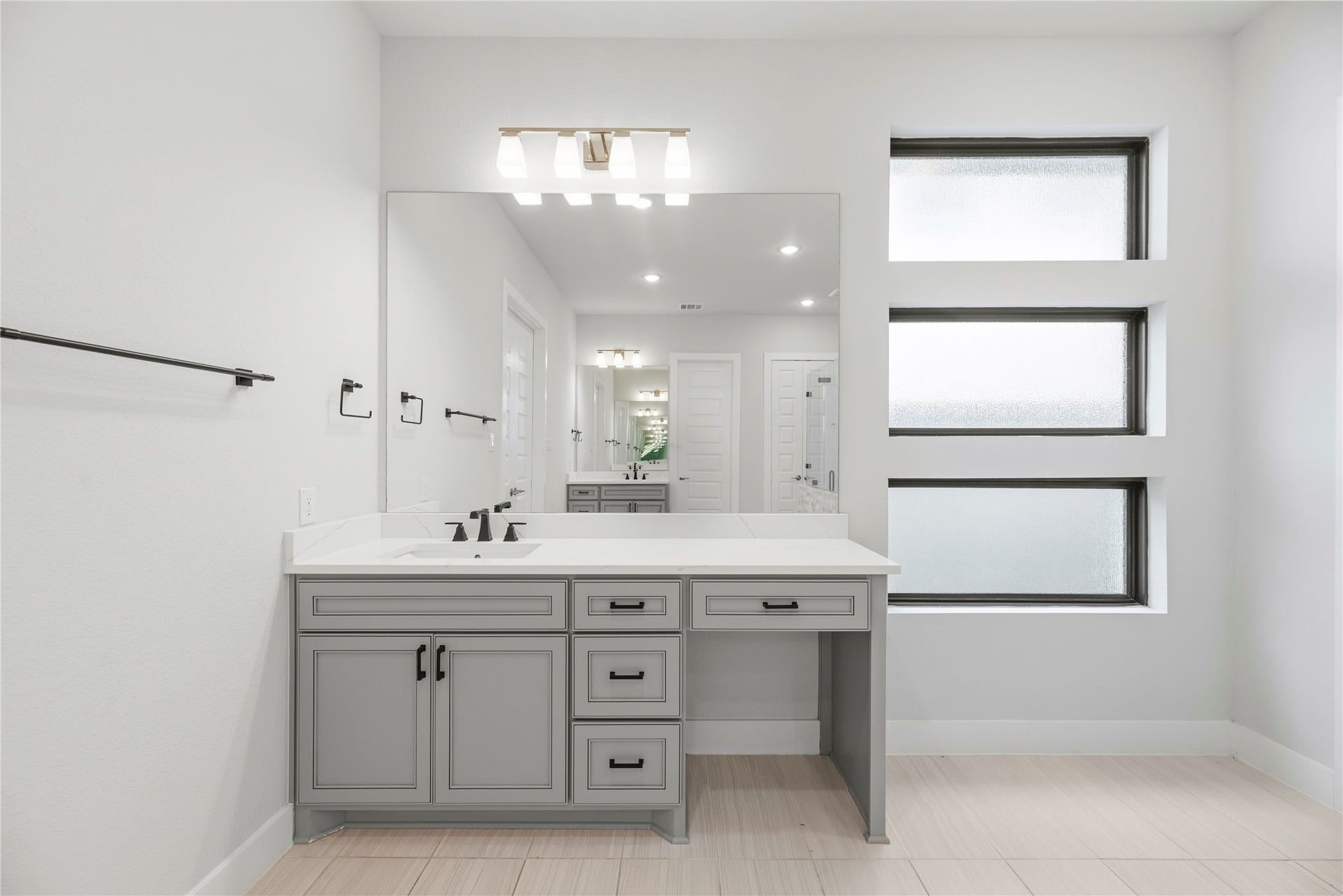 Custom grey vanity unit equipped with quartz countertop, under-mount sink, integrated seated makeup vanity area, and contemporary bath lighting.