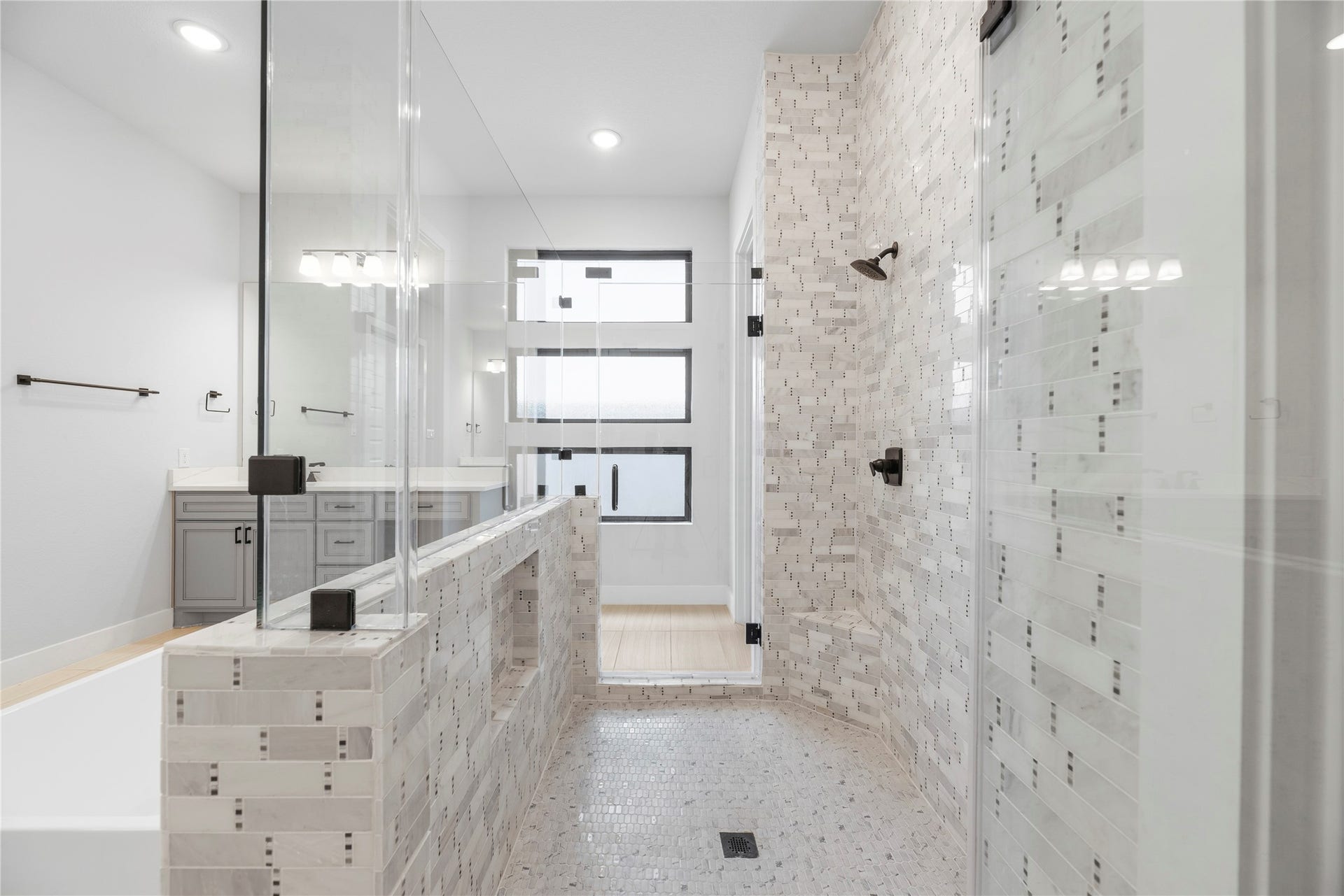 Deluxe tiled walk-in shower complete with dual shower heads, mosaic tile detailing, built-in seating bench, and sleek frameless glass enclosure.